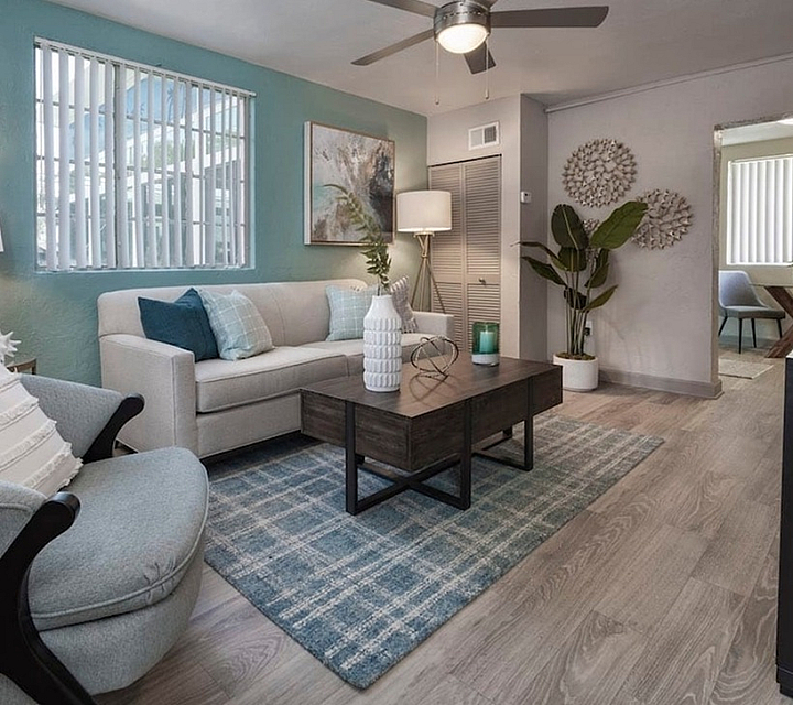 Elegant living room with modern decor, featuring a cozy beige sofa, stylish armchair, and a sleek wooden coffee table. Soft lighting, artistic wall art, and a vibrant potted plant add warmth to the space. The dining area is visible through