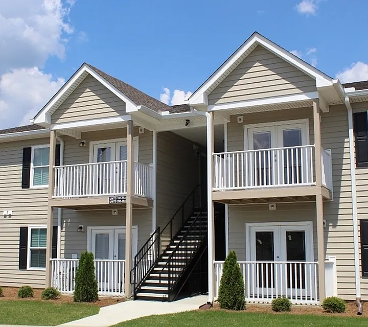 Charming two-story apartment building with stylish beige siding, inviting balconies, and well-maintained landscaping under a bright blue sky.