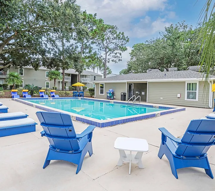Inviting apartment community pool area with vibrant blue lounge chairs and lush green surroundings, perfect for relaxation and leisure.