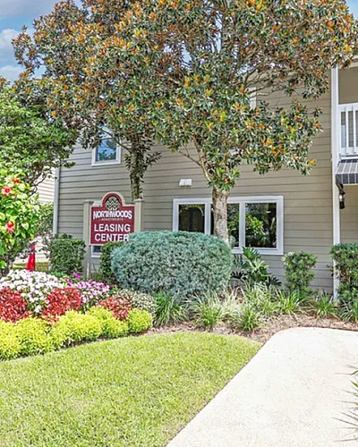 Charming leasing center with vibrant garden and inviting entrance, framed by lush greenery and modern architecture.