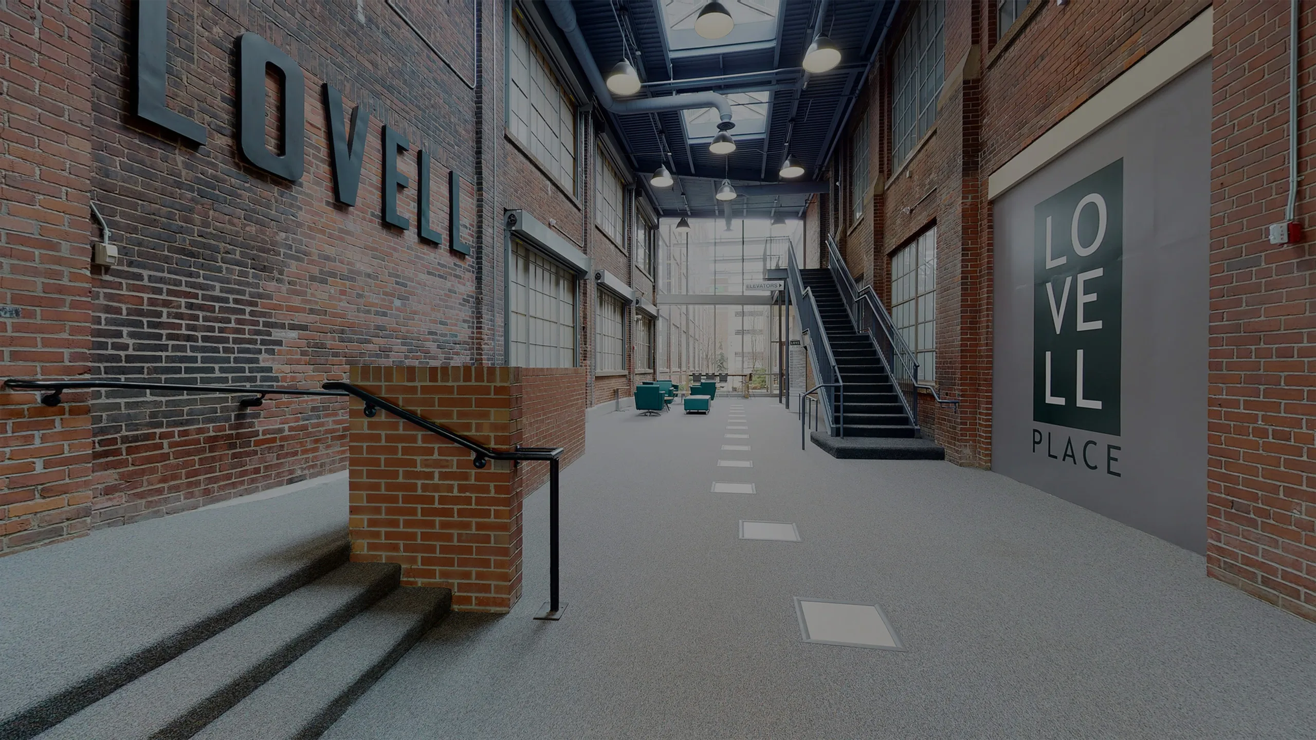 Bright and welcoming lobby with industrial charm, featuring exposed brick walls, high ceilings, and sleek modern stairs.