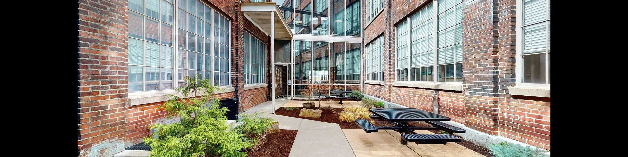 Charming urban courtyard with modern picnic tables, lush greenery, and industrial brick facade for a perfect outdoor retreat.