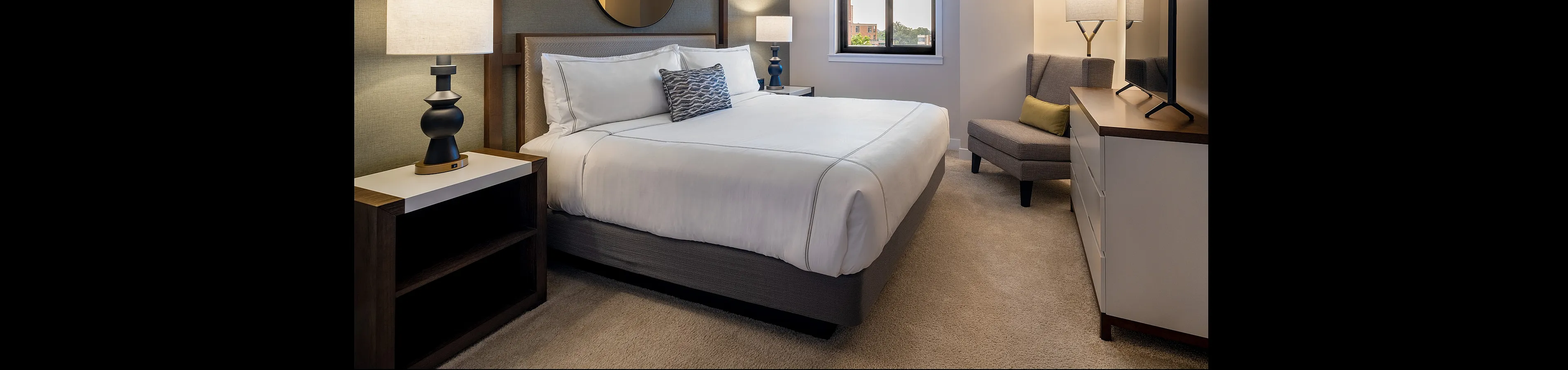 Elegant bedroom with plush carpet, a cozy bed, stylish modern lamps, and a large window offering natural light.
