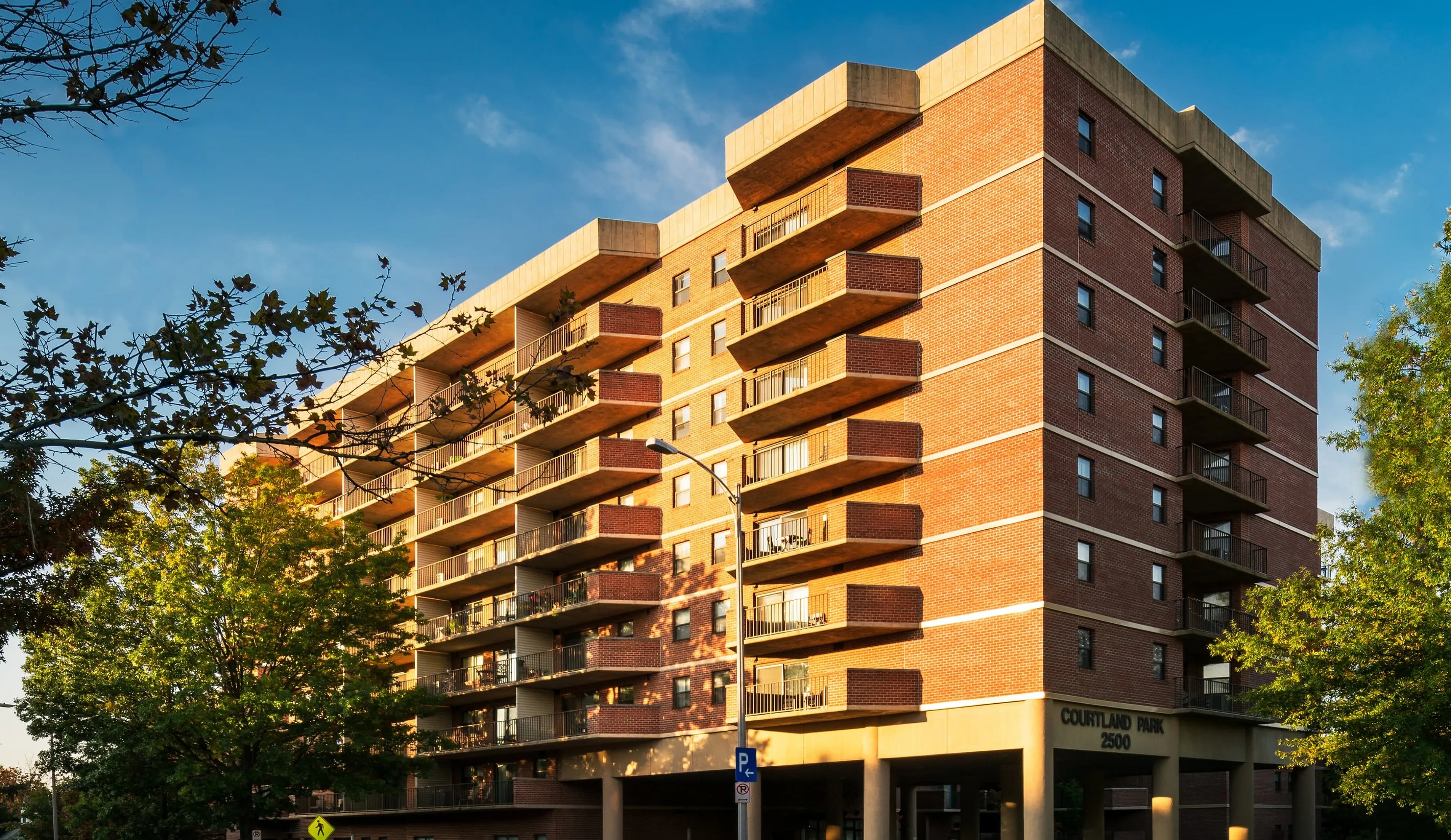 Charming brick apartment building with spacious balconies and lush greenery under a clear blue sky.