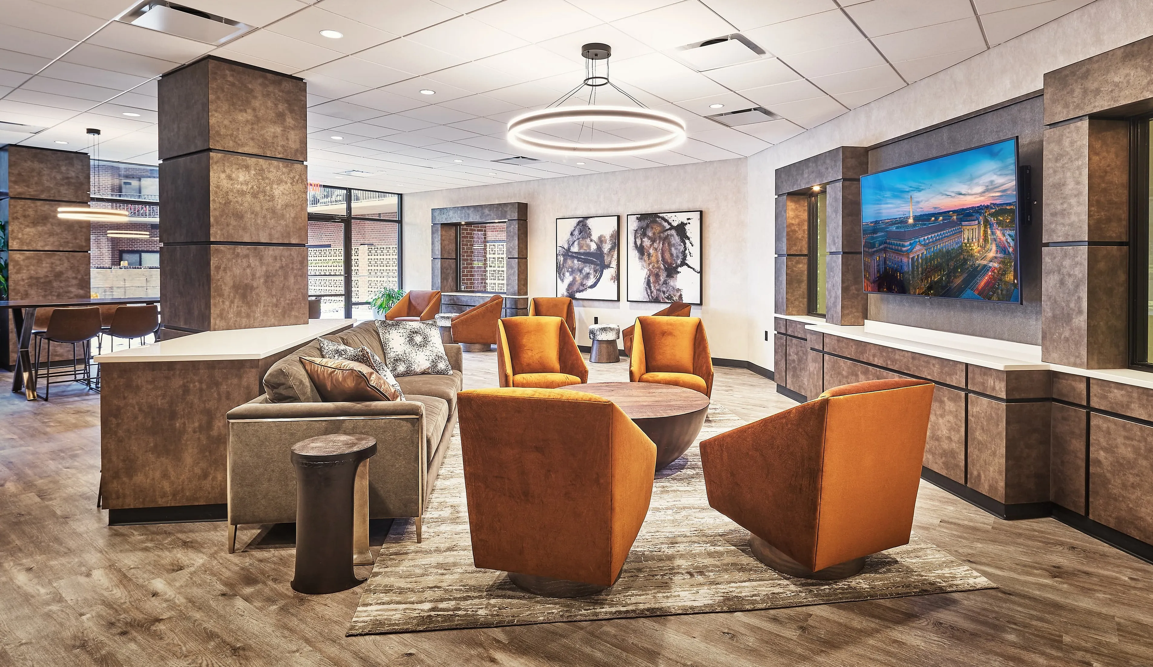 Modern lounge area with elegant orange armchairs, contemporary artwork, and a sleek wooden floor, creating a warm and inviting atmosphere.