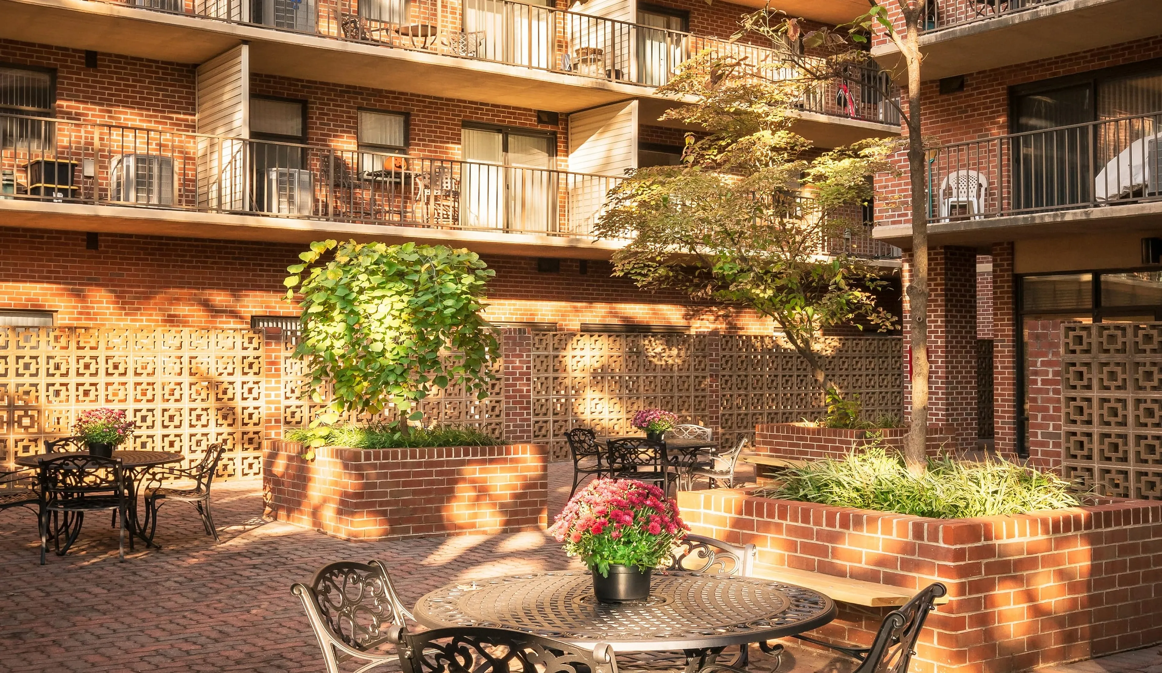 Charming apartment complex showcasing sunlit balconies overlooking a beautifully landscaped courtyard with elegant seating and vibrant greenery.