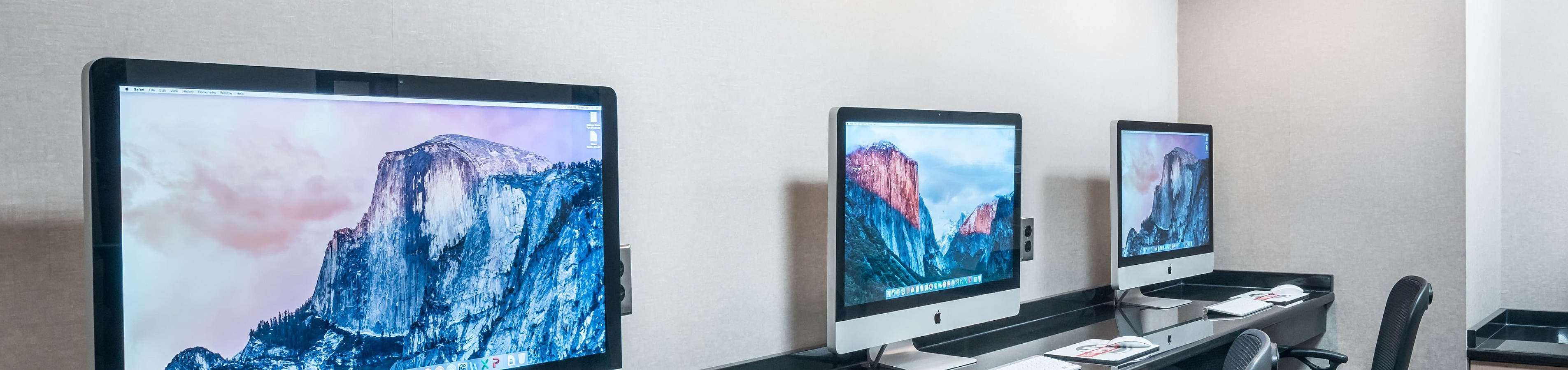 Modern workspace featuring sleek Apple computers, ergonomic chairs, and convenient printer in a well-lit office setting.