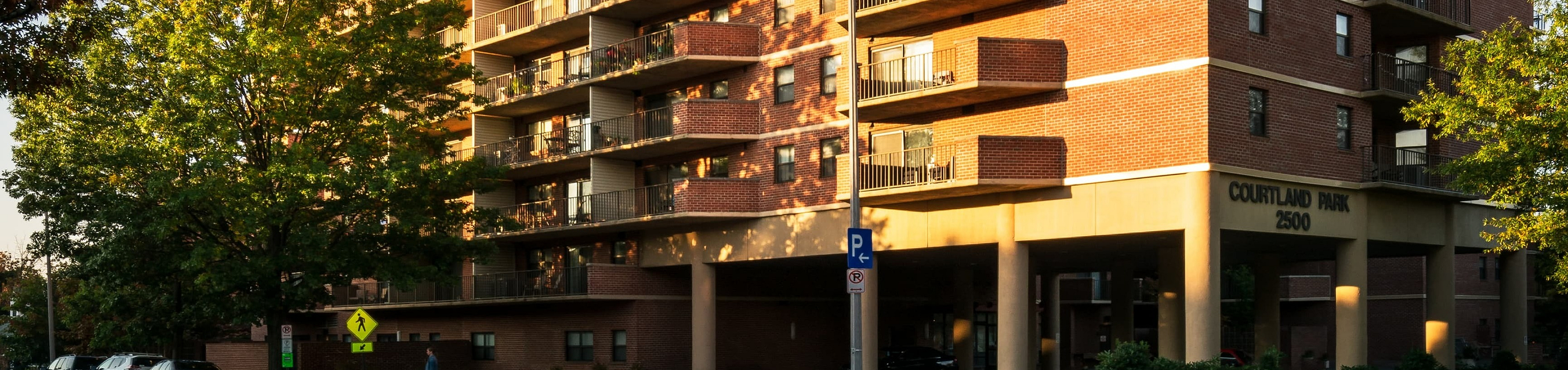 Elegant red-brick apartment building with spacious balconies and lush surroundings basking in warm sunlight.