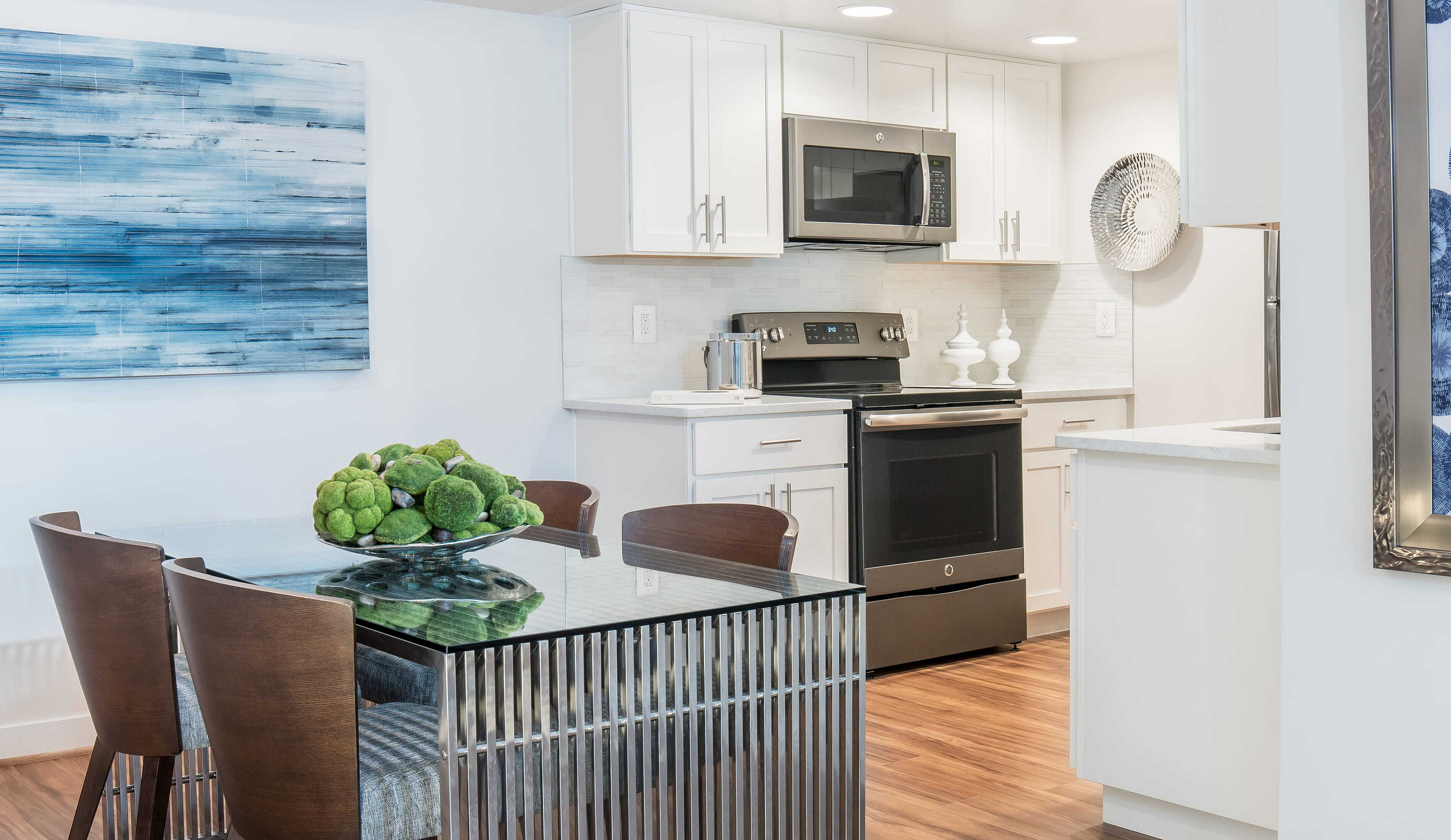 Contemporary dining area with elegant glass table, cozy chairs, and modern kitchen complete with stainless steel appliances and stylish decor.