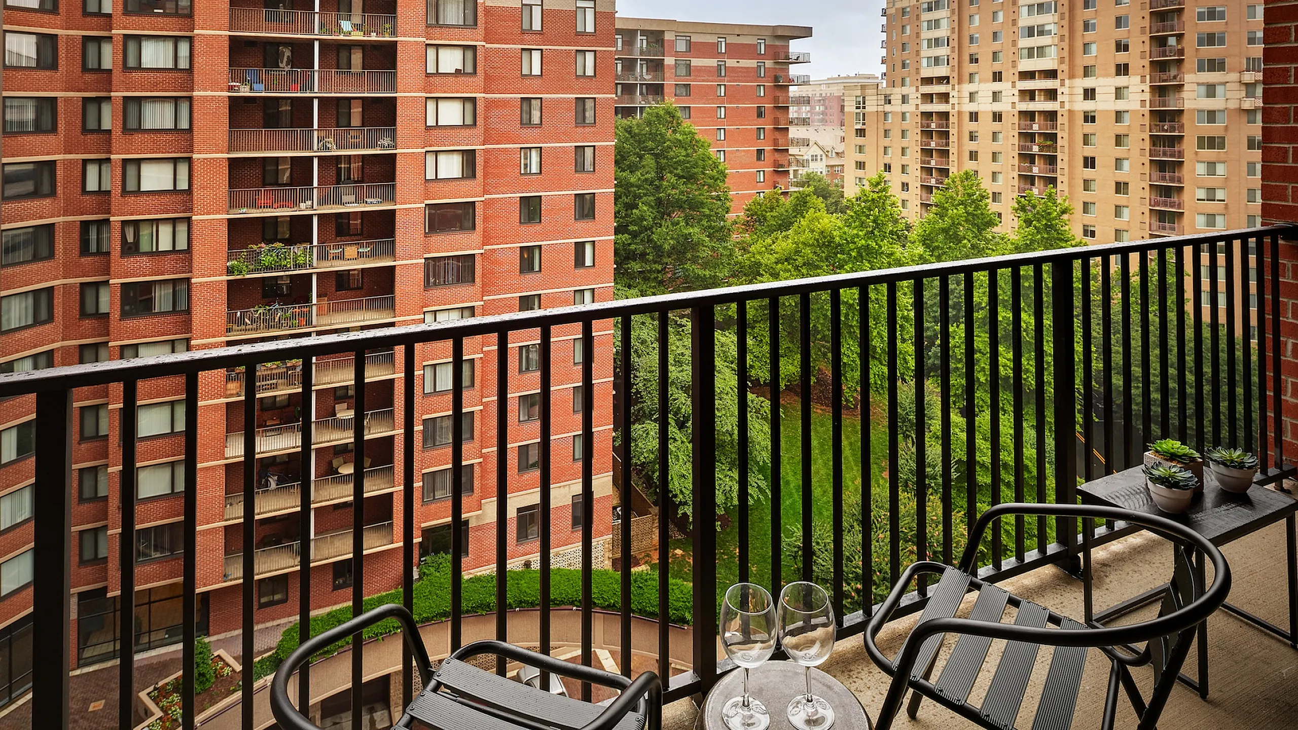 Charming urban balcony view featuring sleek outdoor seating, lush greenery, and elegant wine glasses for a perfect relaxation spot.