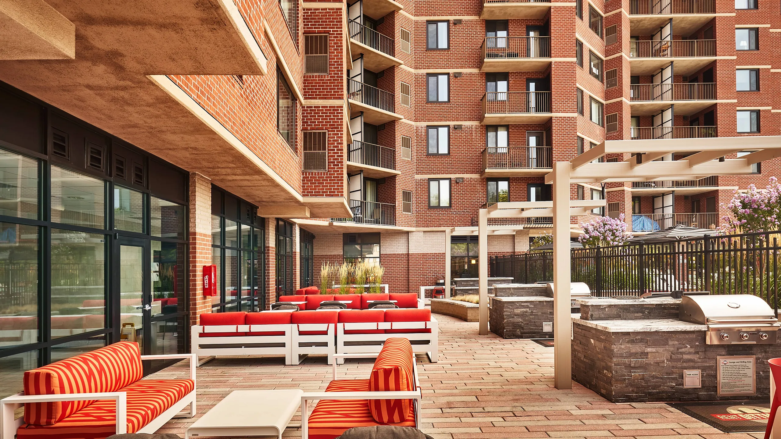 Modern apartment complex with spacious outdoor patio, vibrant seating, and built-in BBQ grills under pergolas.