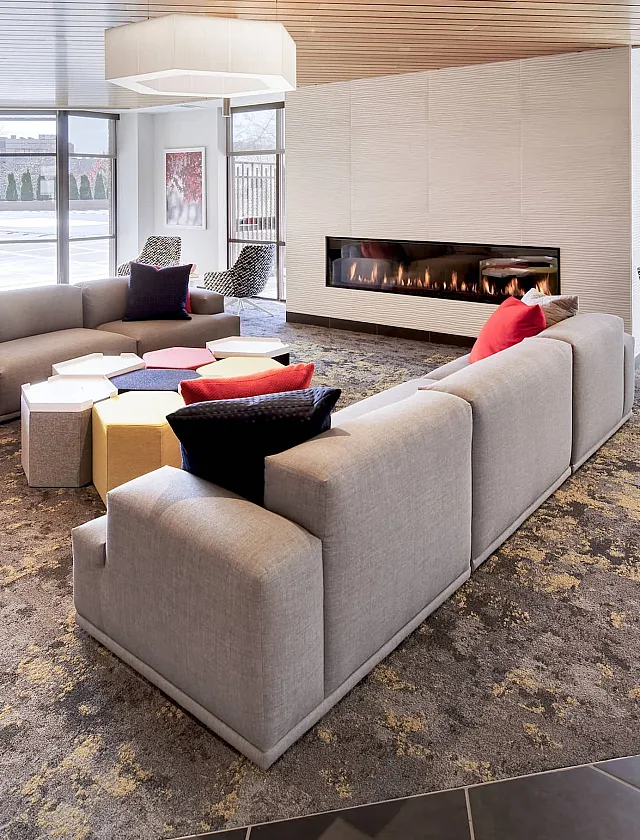 Elegant lounge area with modern L-shaped sofas, cozy fireplace, and large windows offering natural light and garden views.