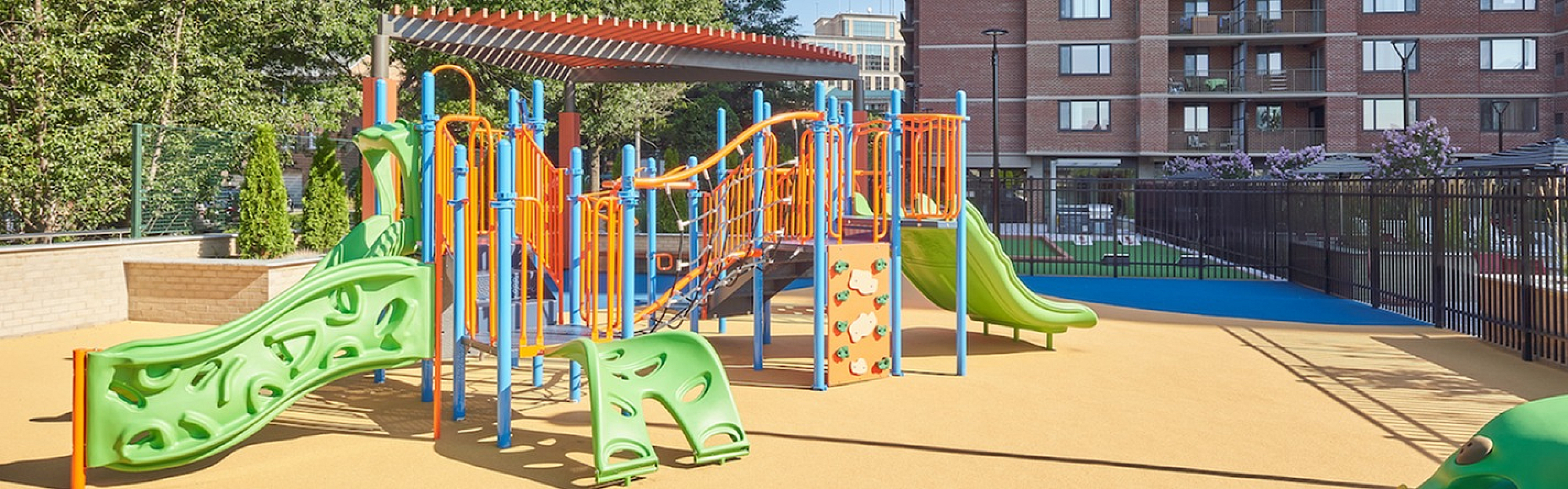 Vibrant outdoor playground with colorful slides and climbing structure set against a modern apartment building backdrop.