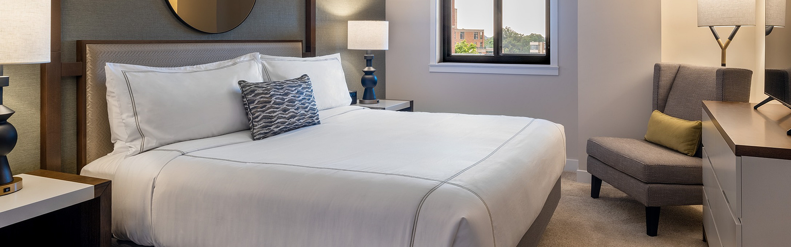 Elegant bedroom featuring a king-sized bed, modern decor, and ample natural light through a large window.