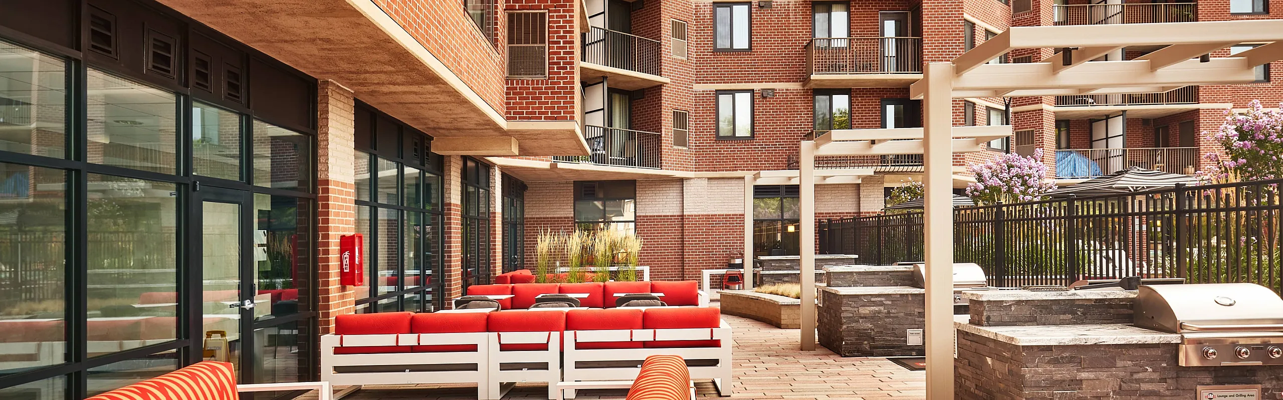 Modern outdoor patio with vibrant seating and barbecue area, set against a stylish red brick apartment complex featuring balconies.
