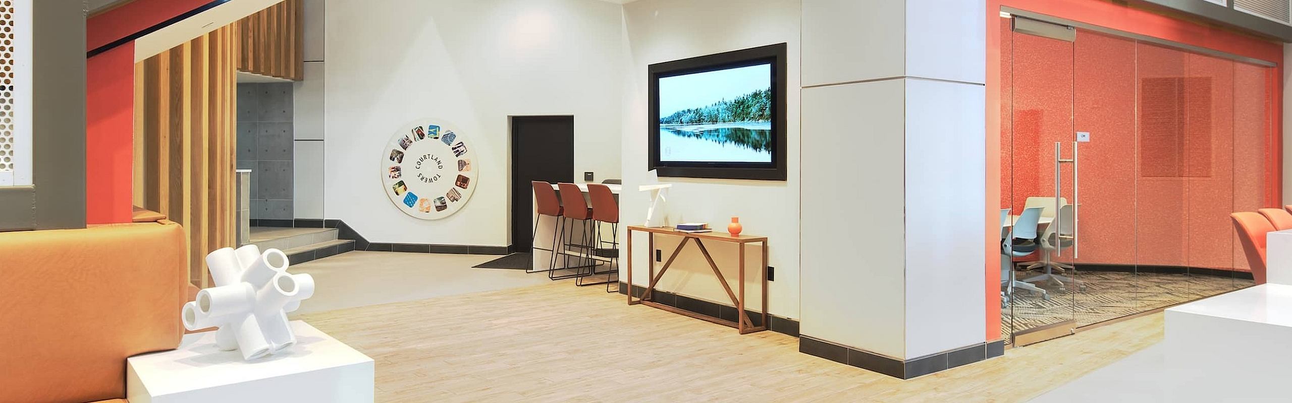 Modern lobby with sleek design featuring orange seating, contemporary art, and chic wooden flooring.