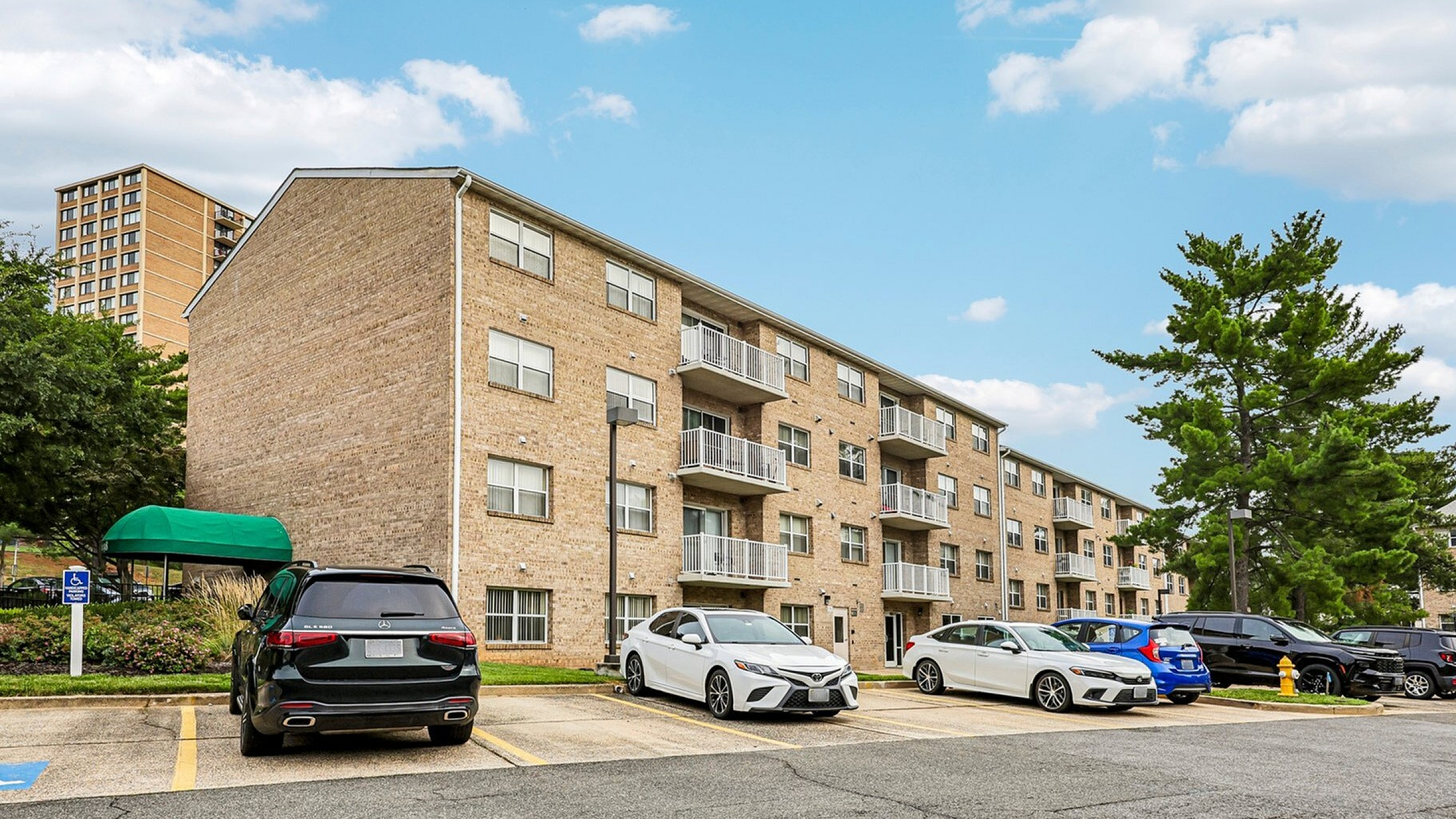 Charming brick apartment complex with spacious balconies and ample parking under a bright blue sky.