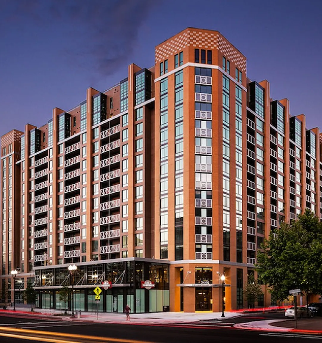 Stunning modern high-rise apartment building with sleek architectural design, illuminated at dusk, showcasing vibrant urban living.