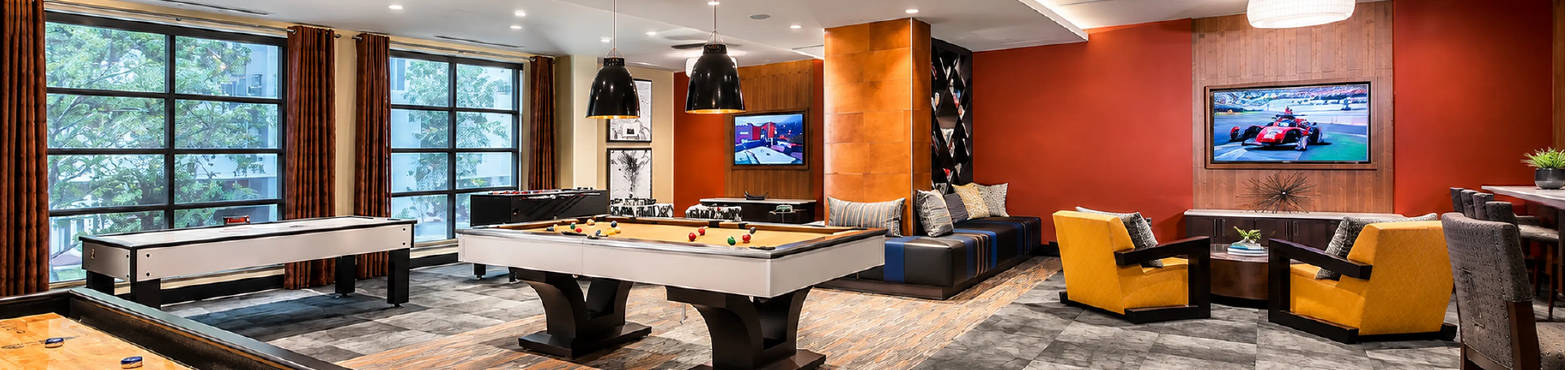 Vibrant and luxurious game room featuring modern pool, shuffleboard, and foosball tables, accented by stylish seating and ambient lighting.
