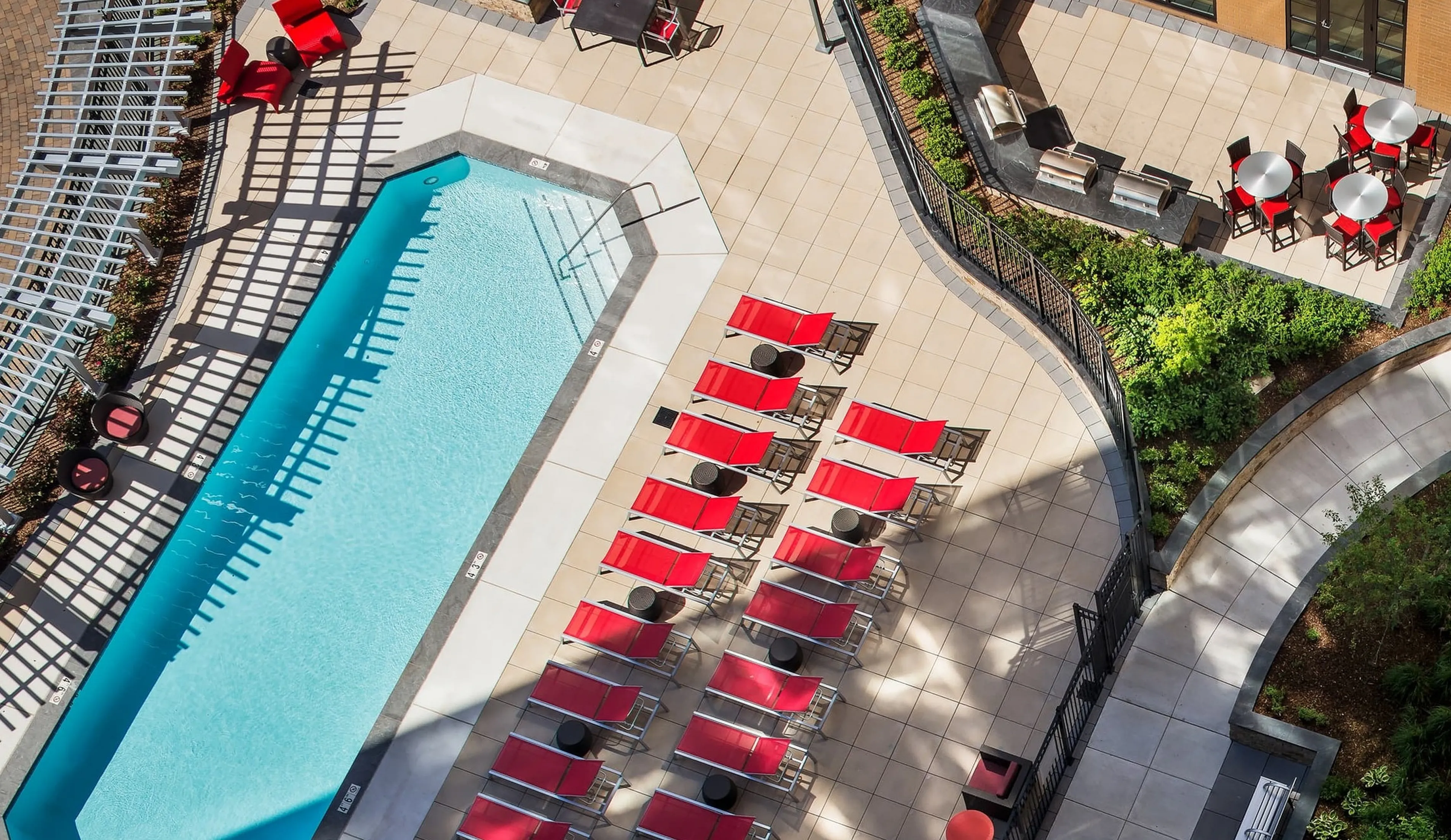 Luxurious poolside oasis with sleek red lounge chairs and elegant patio seating, perfect for relaxation and entertaining.