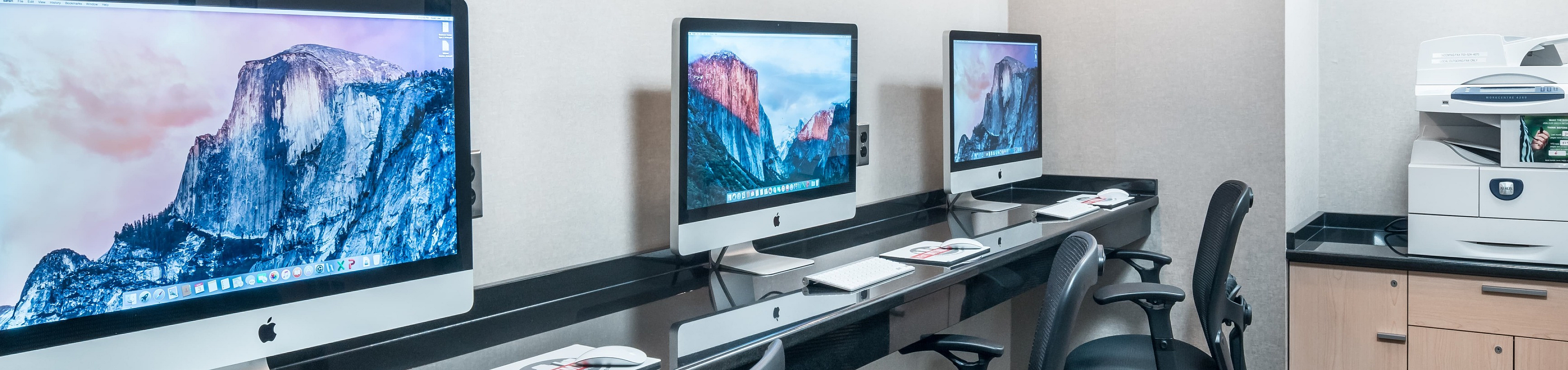 Sophisticated office space featuring sleek desks with modern iMacs and ergonomic chairs, complemented by a multifunctional printer.