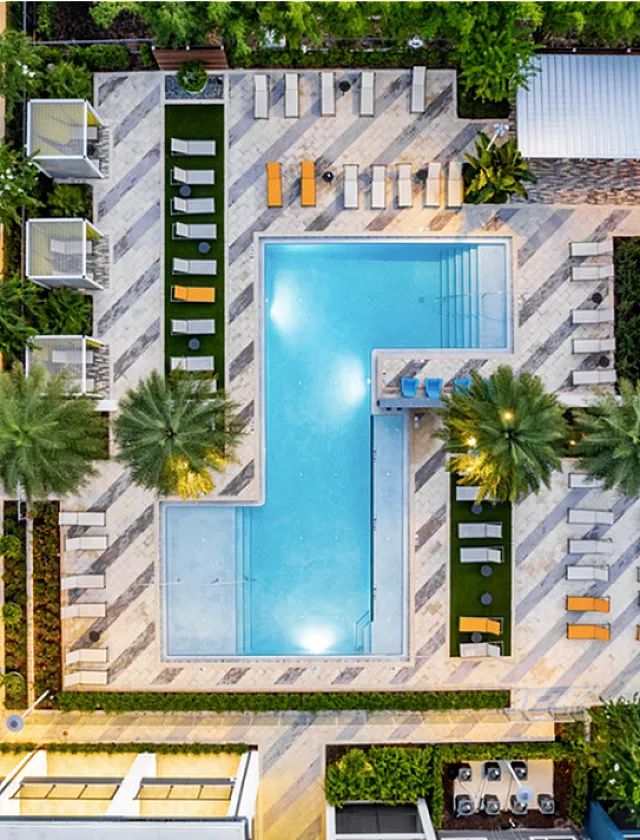 Aerial view of a stylish apartment complex pool area surrounded by palm trees and sun loungers.