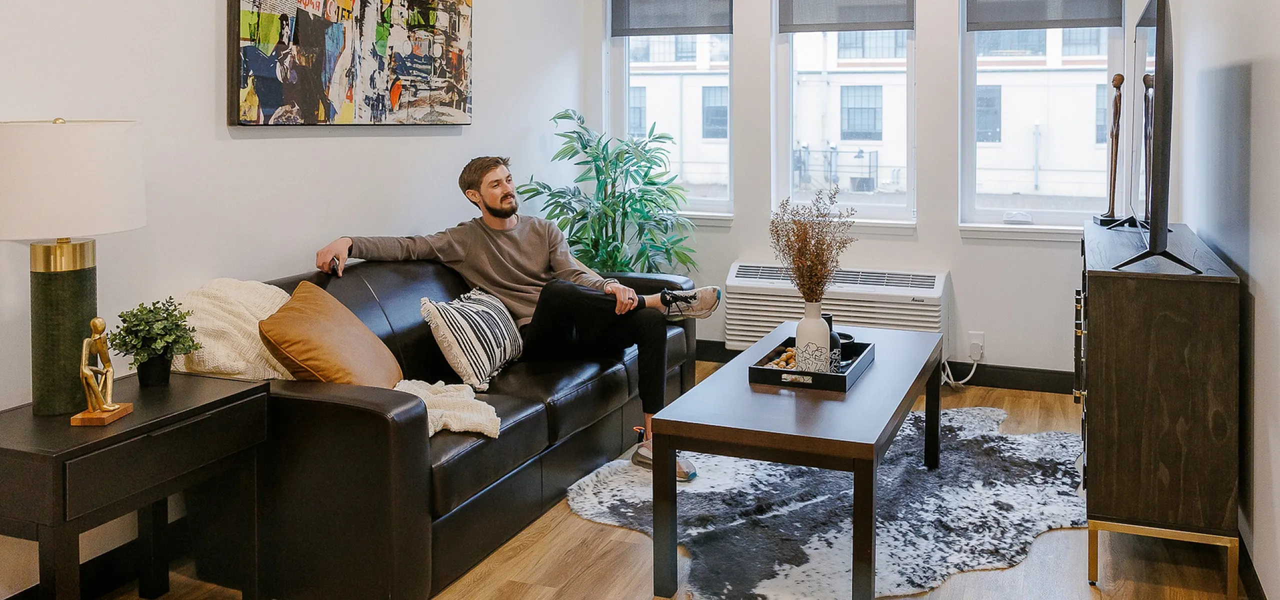 Cozy modern living room with sleek leather sofa, vibrant abstract art, and large windows offering natural light.