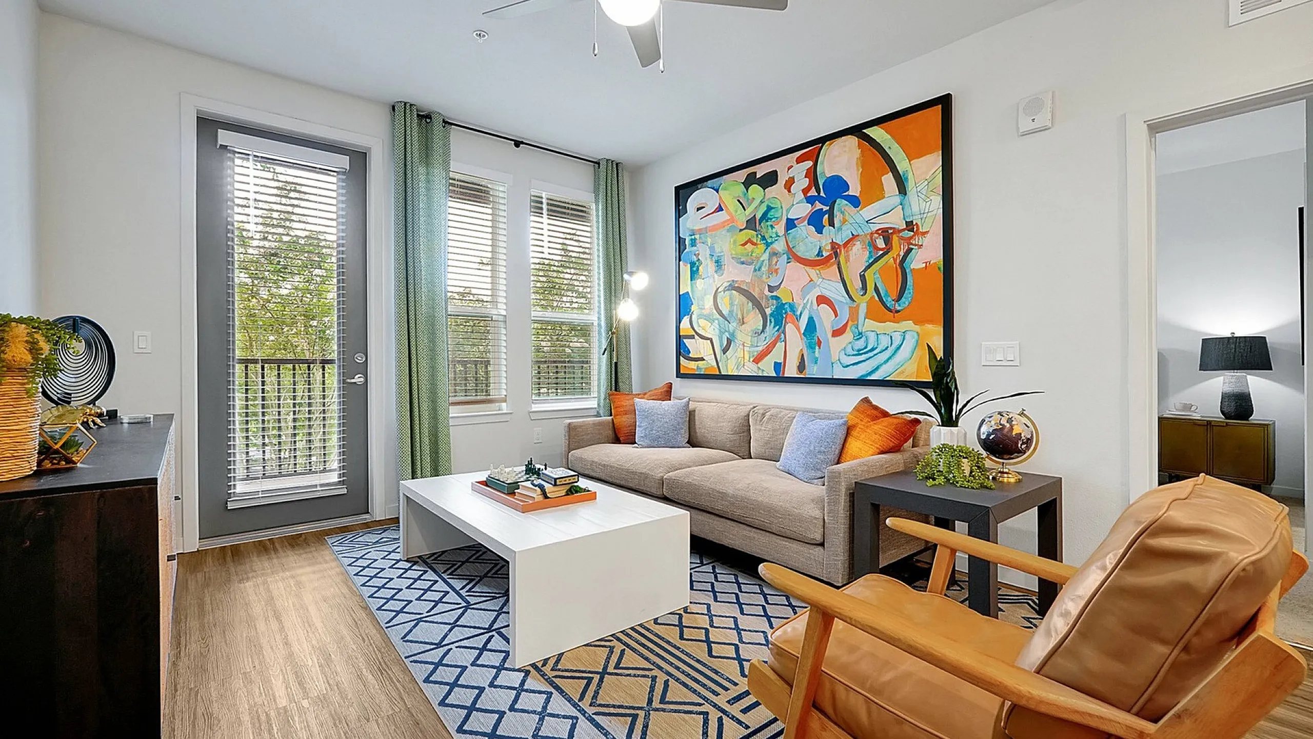 Inviting living room with modern decor, vibrant artwork, cozy sofa, and natural light from large windows.
