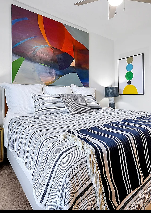 Bright and modern bedroom featuring elegant lighting, cozy striped bedding, and vibrant abstract artwork.