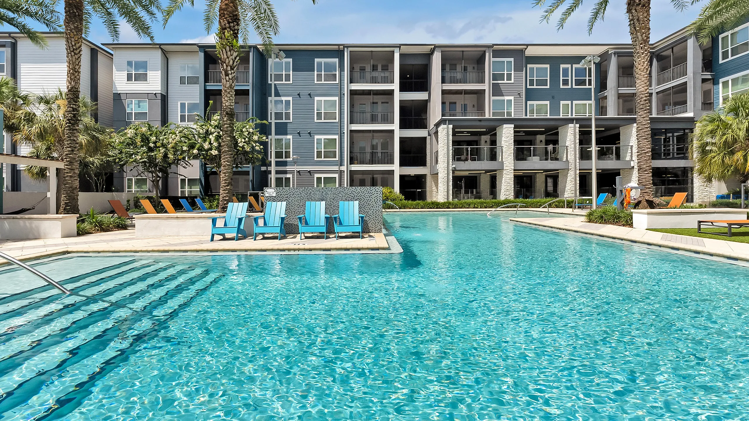 Luxurious apartment complex featuring a pristine swimming pool, surrounded by vibrant greenery and modern architecture.