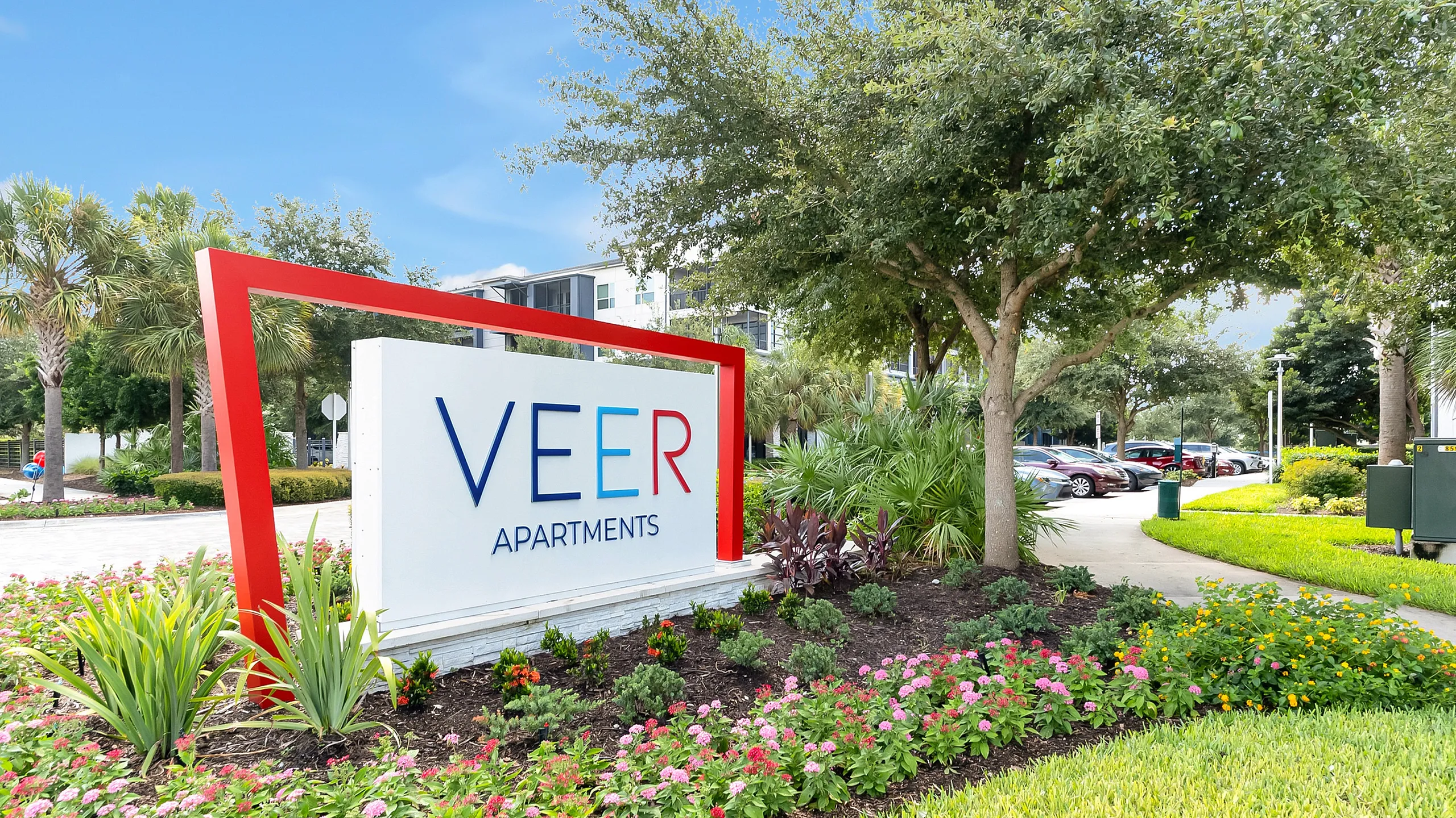 Inviting entrance to Veer Apartments surrounded by lush landscaping and vibrant flowers.