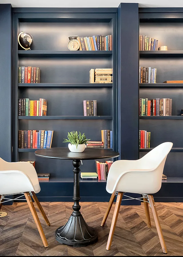 Chic reading nook with elegant navy blue bookshelves, modern white chairs, and a stylish round table with a potted plant.