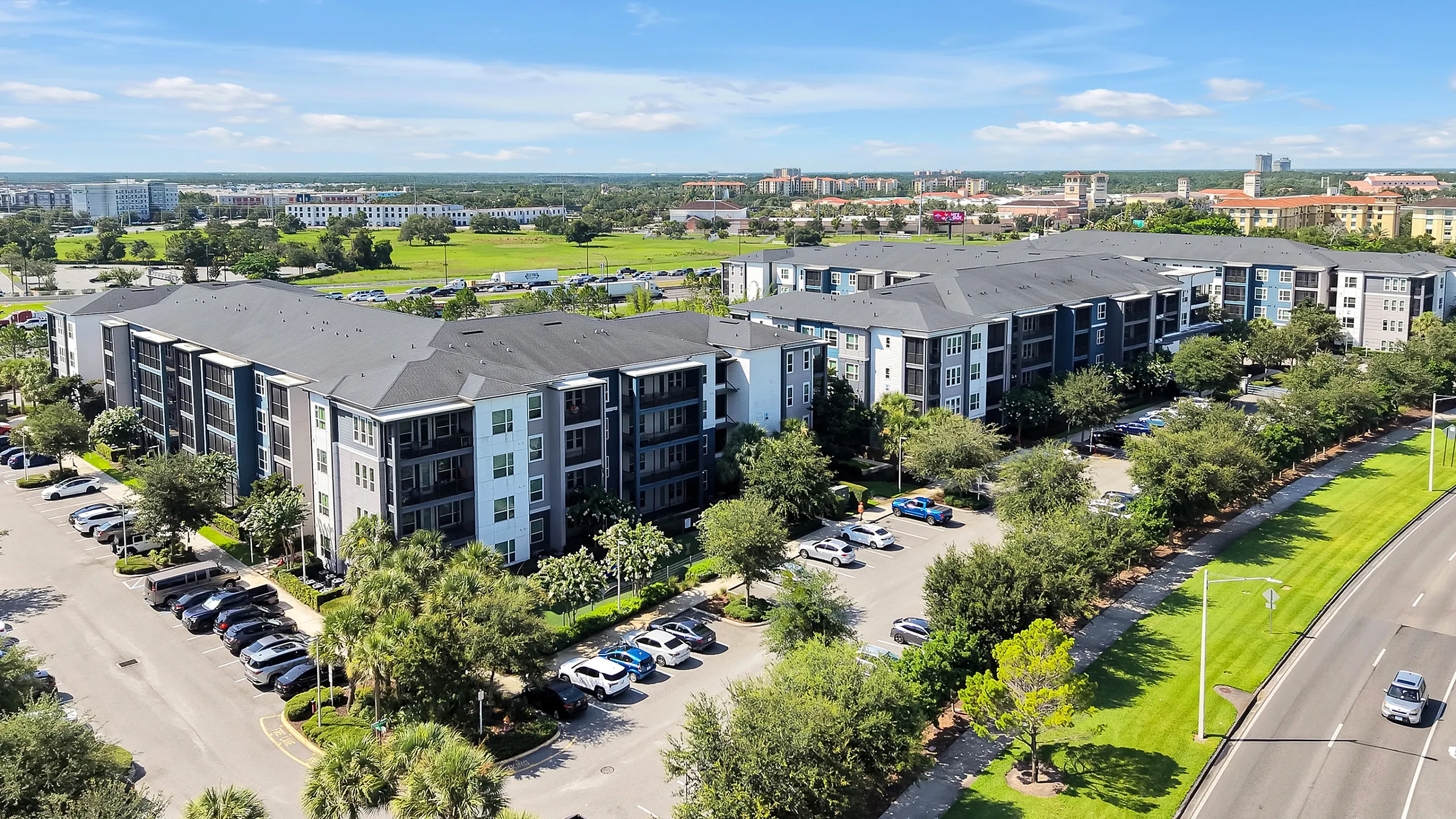Aerial view of a modern apartment complex surrounded by lush greenery and ample parking, offering convenience and serene living.