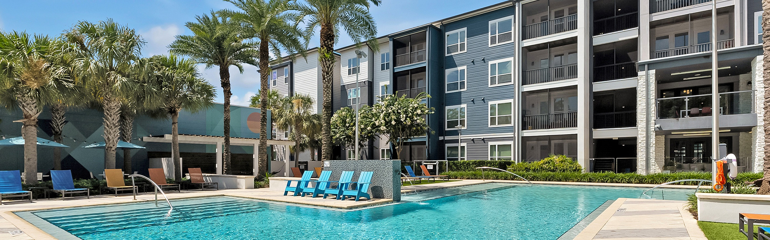 Luxurious apartment complex showcasing a sparkling outdoor pool surrounded by palm trees, modern lounge chairs, and sleek architecture.