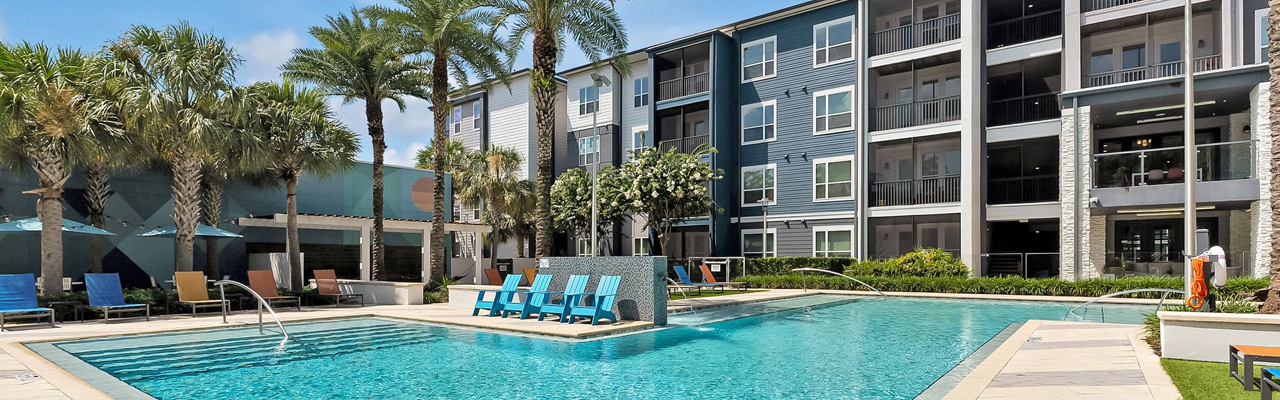 Luxurious apartment complex with a sparkling outdoor pool, surrounded by palm trees and stylish lounge chairs, perfect for relaxation.