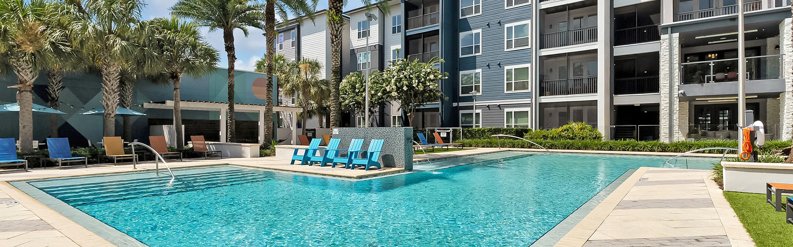 Luxurious apartment complex with a stunning resort-style pool surrounded by palm trees and modern lounging areas.
