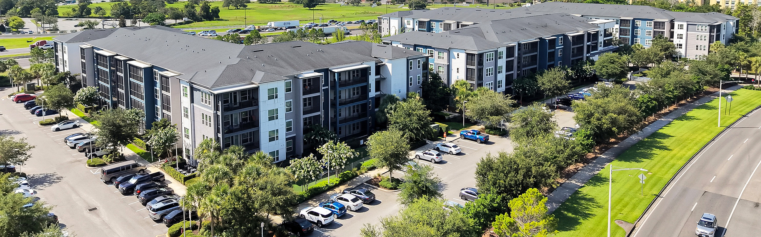 Aerial view of a modern apartment complex with lush landscaping, ample parking, and a serene suburban setting.
