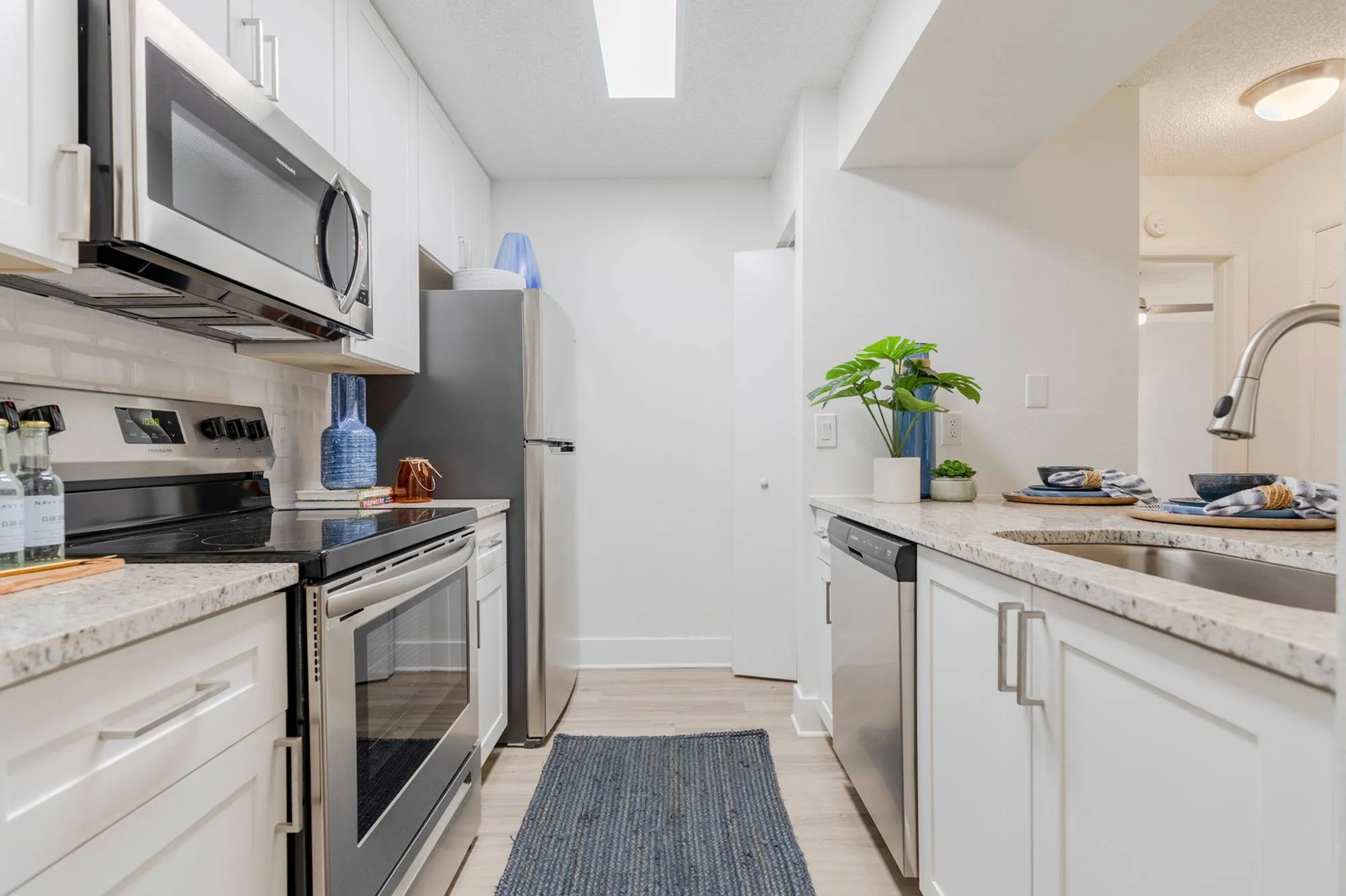 Apartments Near University Park - Tradition at Palm Aire - Kitchen With White Cabinets, Stainless-Steel Appliances, Vinyl Plank Flooring, And Granite Kitchen Countertops.