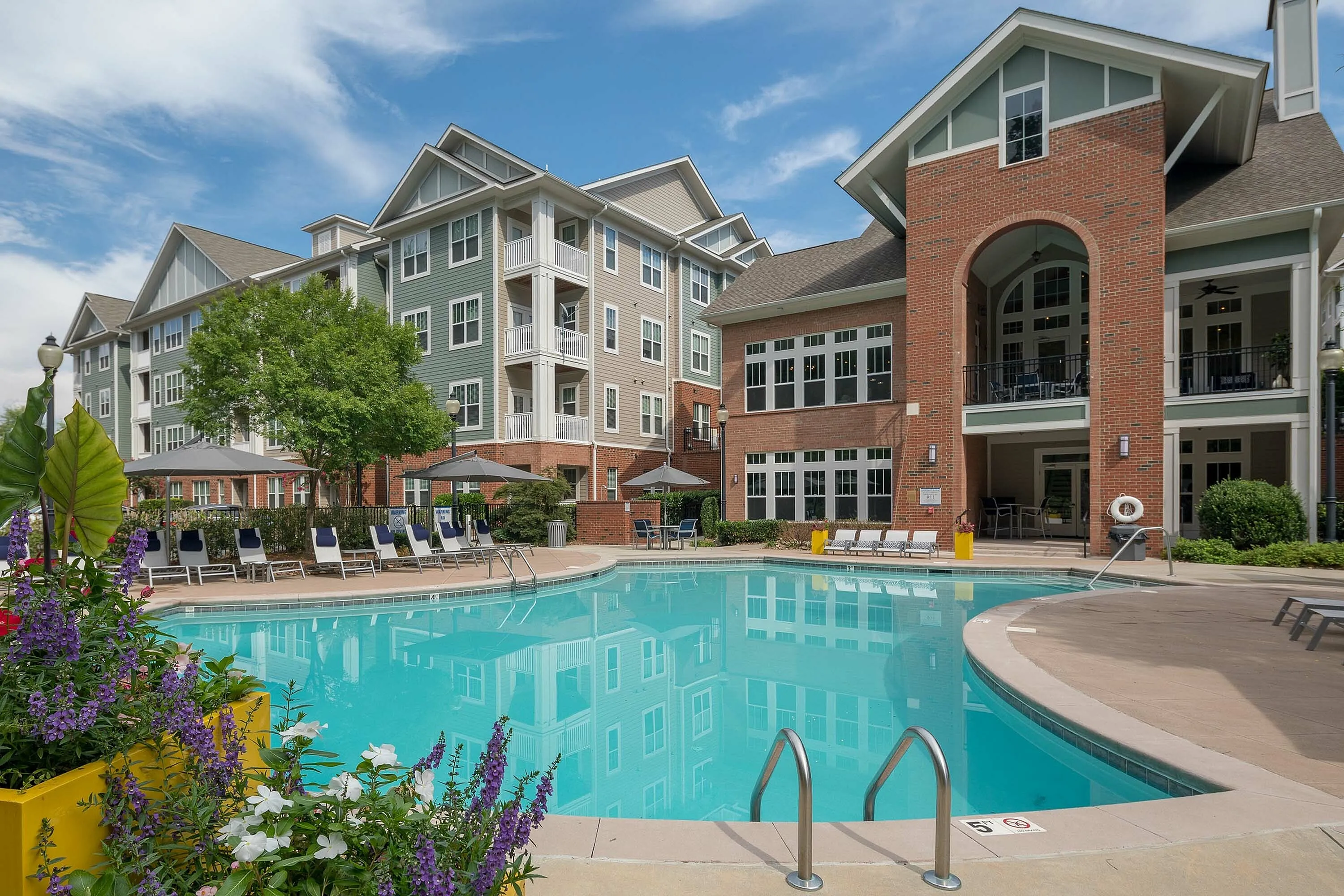 Chic apartment complex with a sparkling outdoor pool, surrounded by flowers and sun loungers.