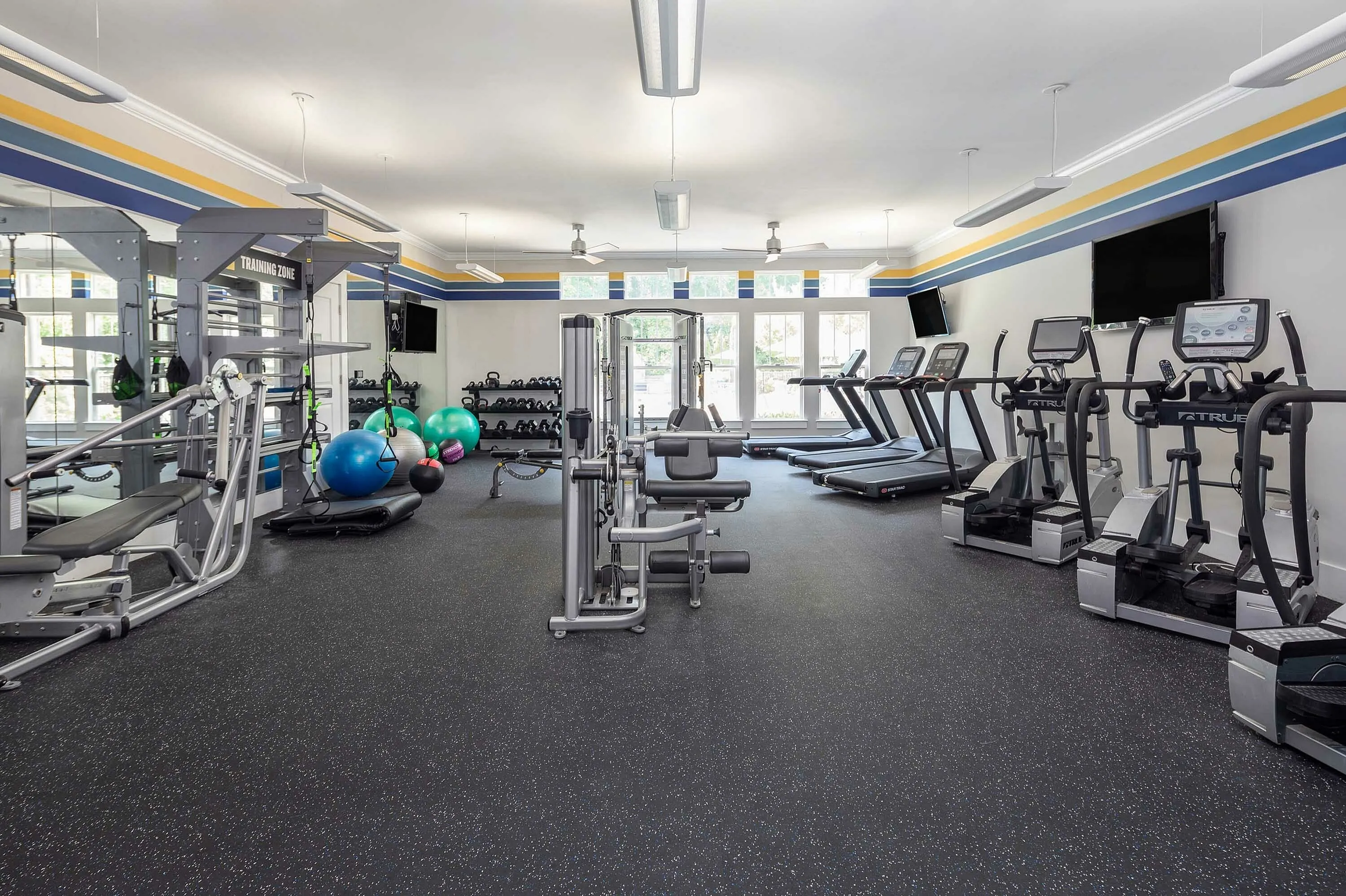 Modern gym with weight machines, treadmills, and exercise balls in a bright, spacious room.