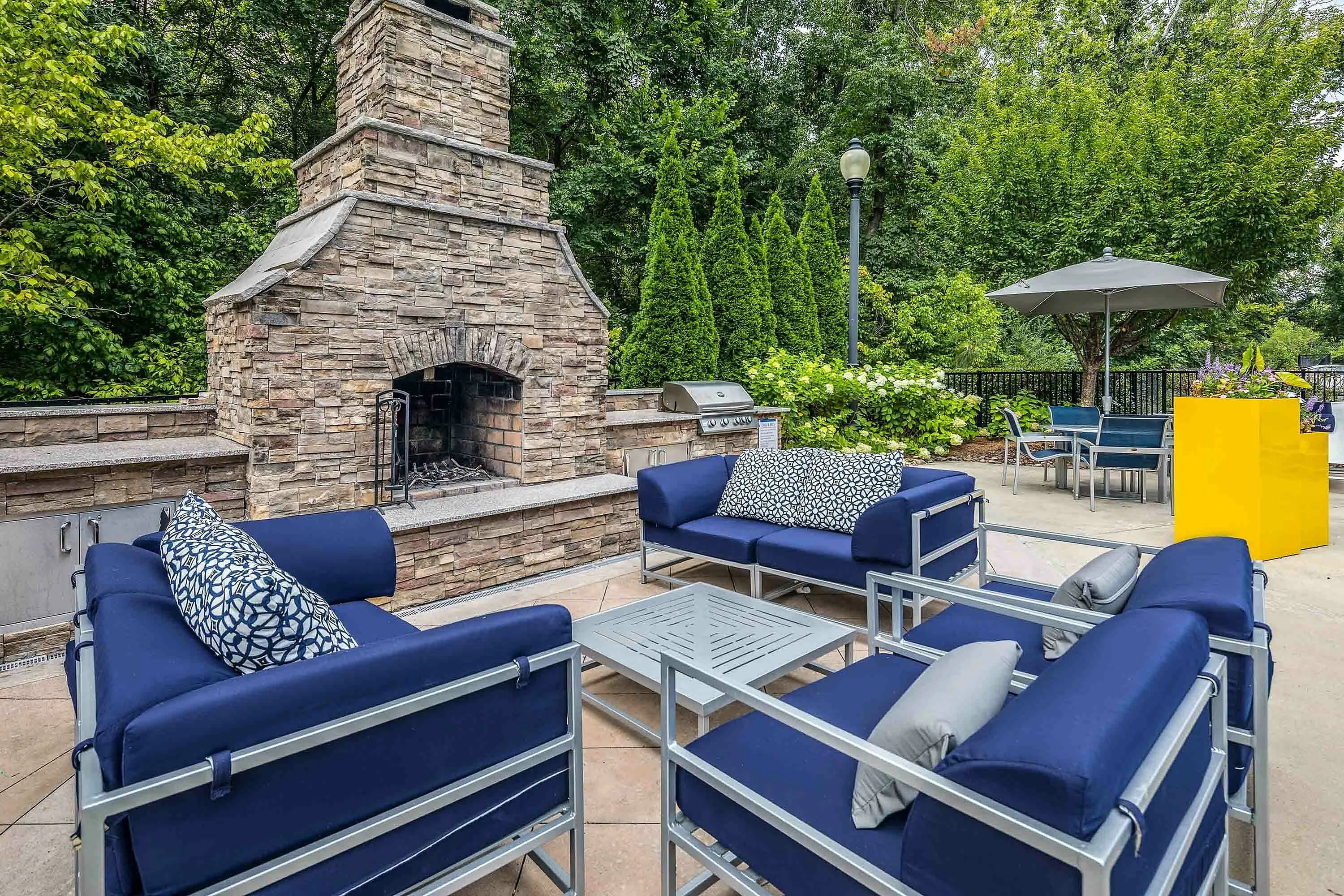 Inviting outdoor patio with blue cushioned seating and a rustic stone fireplace.