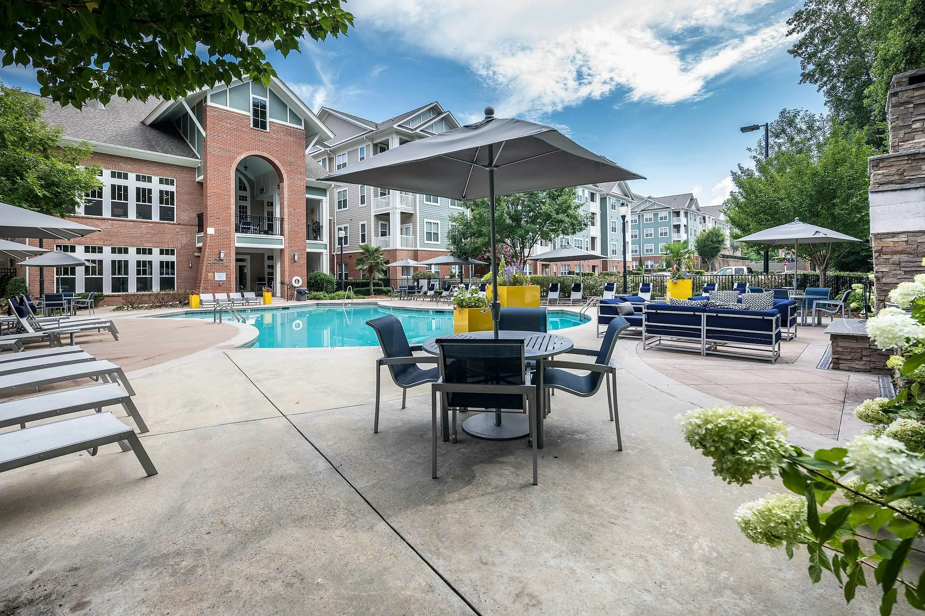 Luxurious apartment complex with a pristine pool, surrounded by modern outdoor furniture and lush greenery.