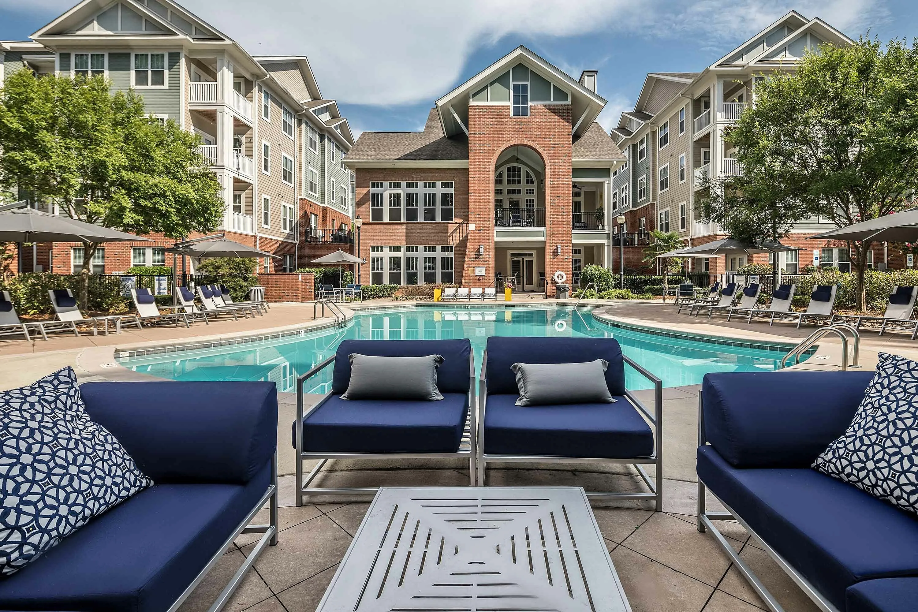 Chic outdoor seating by a large swimming pool surrounded by stylish apartment buildings.