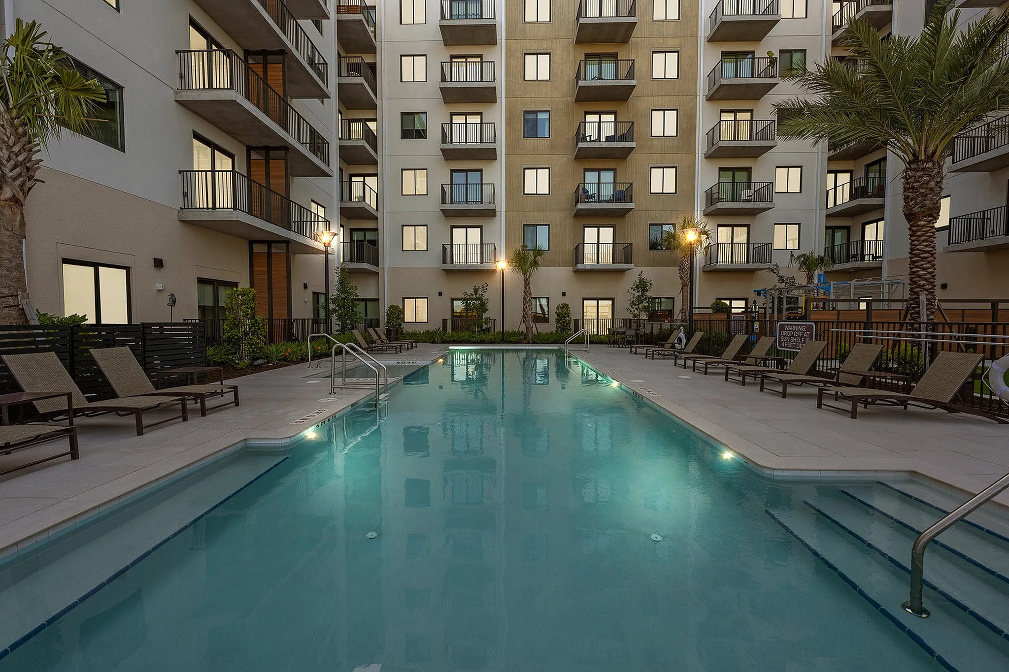 2-Bedroom Luxury Apartments Viera FL - Luna At Viera - Exterior Shot Of The Resort-Style Swimming Pool Surrounded By Palm Trees And Lounge Chairs