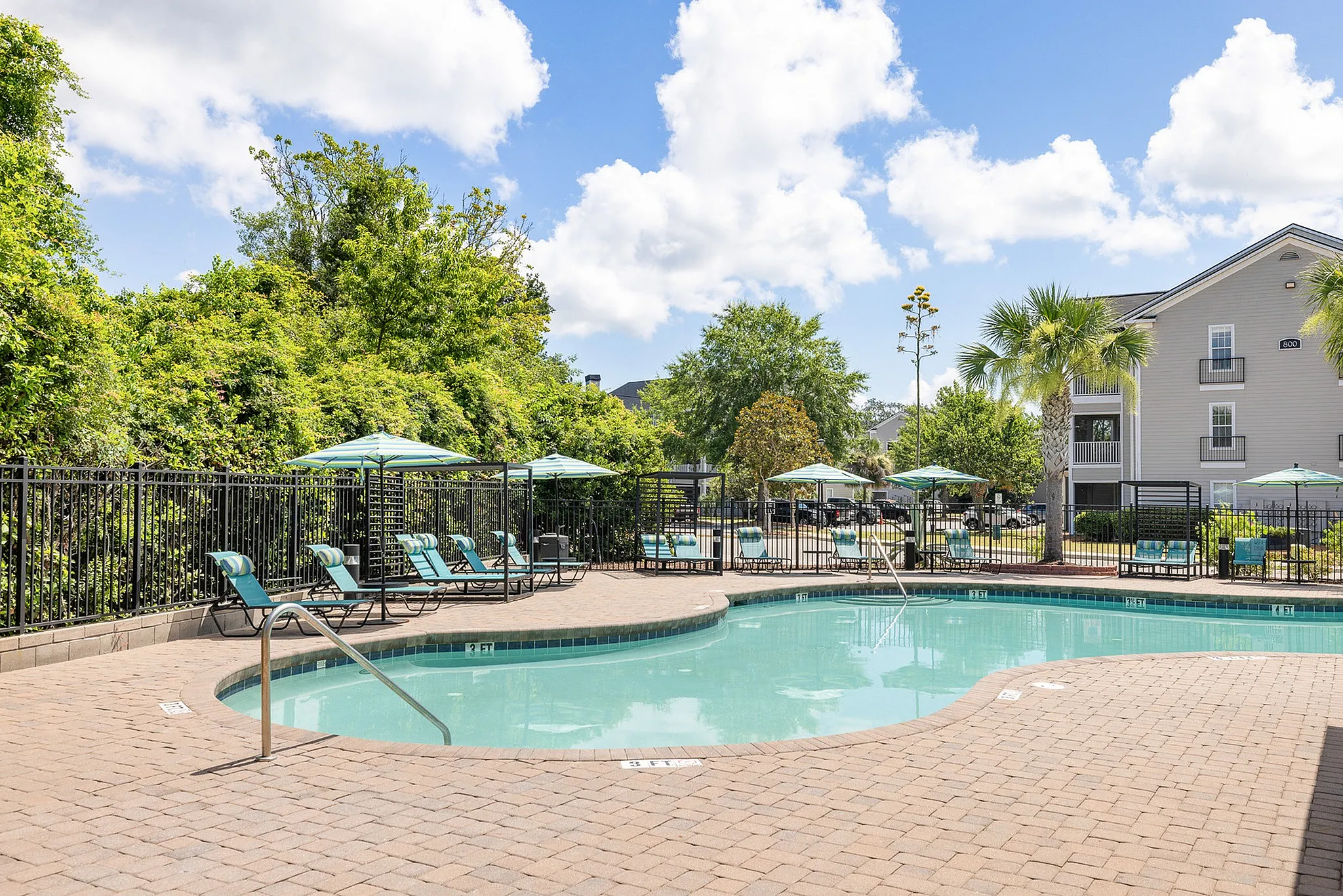 Port Royal, SC, Apartments Near Air Station - Preserve at Port Royal - Resort Style Swimming Pool With Paver Sundeck, Lounge Chairs, Shade Umbrellas, Palm Trees, And Community Buildings.