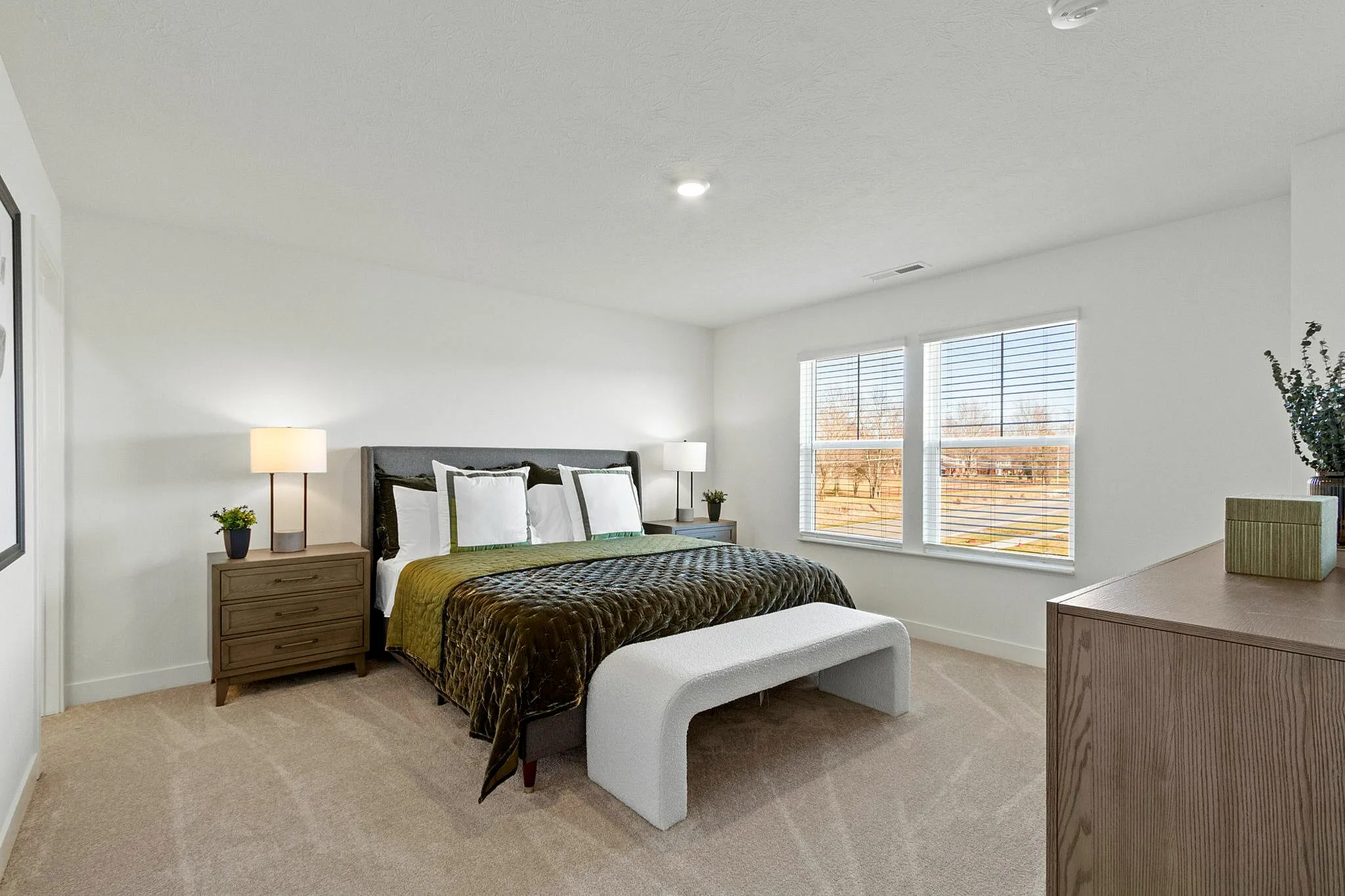 Townhomes in Brownsburg, IN, with In-Unit Washer and Dryer - Wynne Farms - Bedroom With Green Throw Blanket, White Bench, Wood Nightstands, And Two Large Windows.