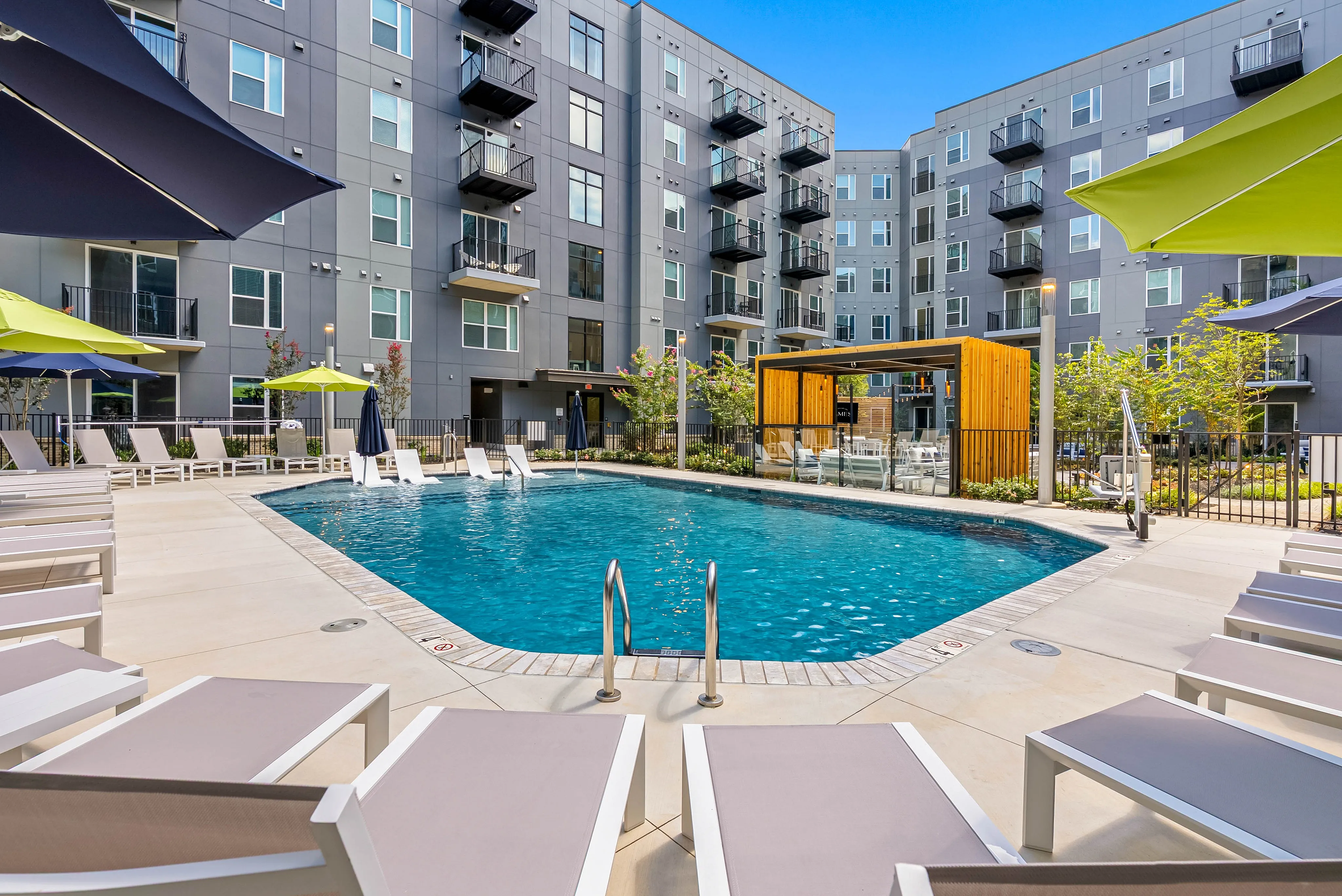 Richmond, VA, Luxury Apartments for Rent - The James at Springline - A Swimming Pool with Lounge Chairs, Umbrellas, Landscaped Areas, and a Modern Apartment building.
