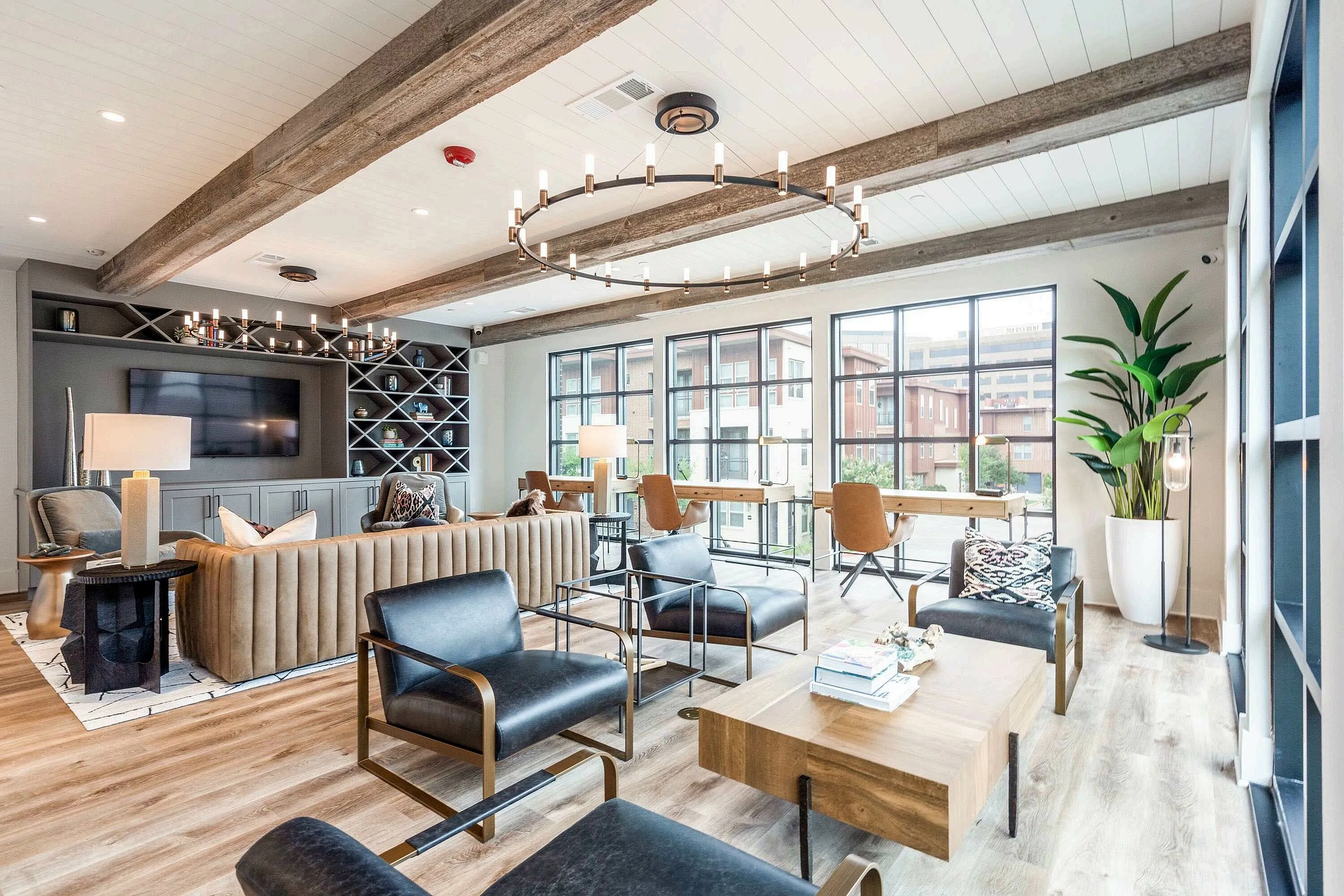 A modern lounge area featuring comfortable seating, wooden beams, and large windows that allow natural light to fill the space. A decorative plant and stylish light fixtures add to the inviting atmosphere.