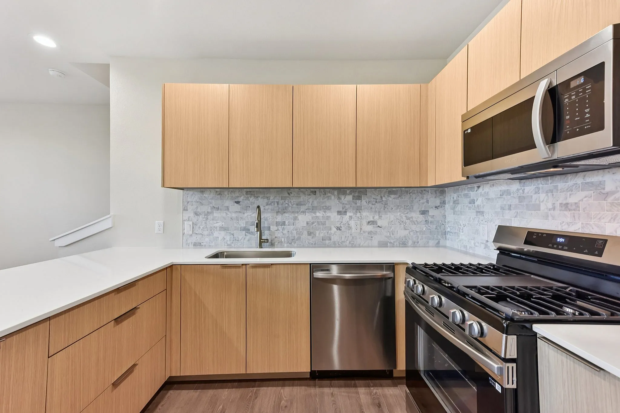 North Austin, TX, Townhomes with Attached Garage - Lone Oak Homes - Modern Kitchen With Quartz Countertops, Tile Backsplash, Flat-Panel Wood Cabinets, And Stainless Steel Appliances.
