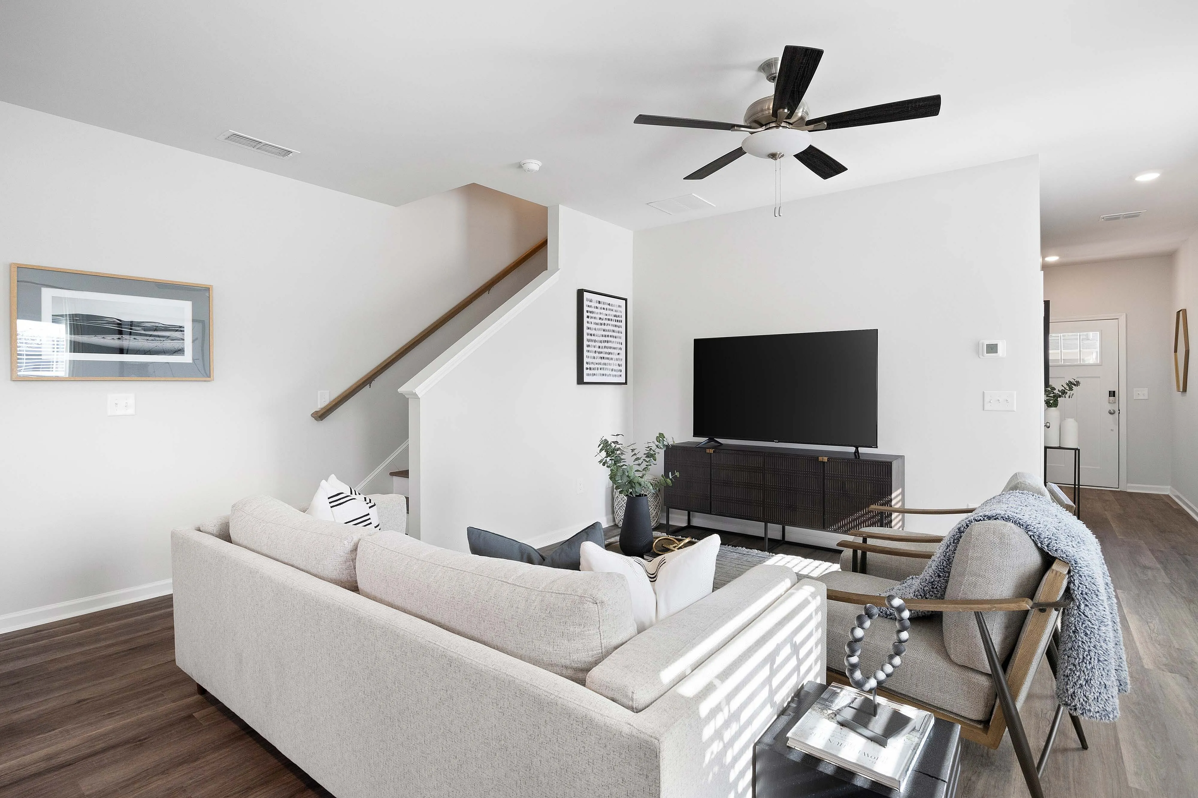 Pet-Friendly Townhomes in Cartersville, GA - Brightside at Cloverleaf - Living Room With Wood-Inspired Luxury Plank Flooring, A Sectional Sofa, Television Console, Armchairs, And A Ceiling Fan.